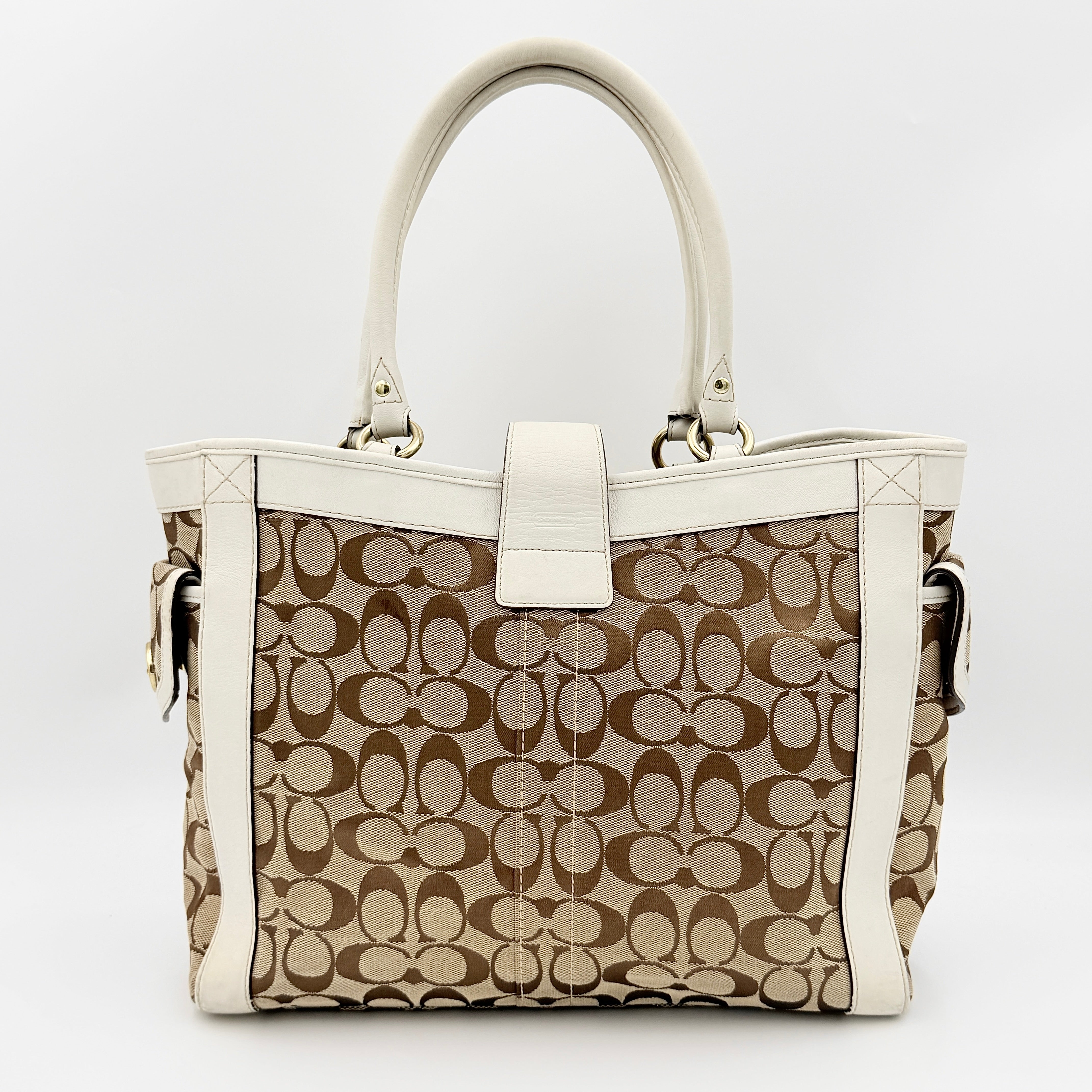 Coach Signature Soho Buckle Tote in beige canvas with white leather trim and gold-tone hardware, displayed against a clean background.