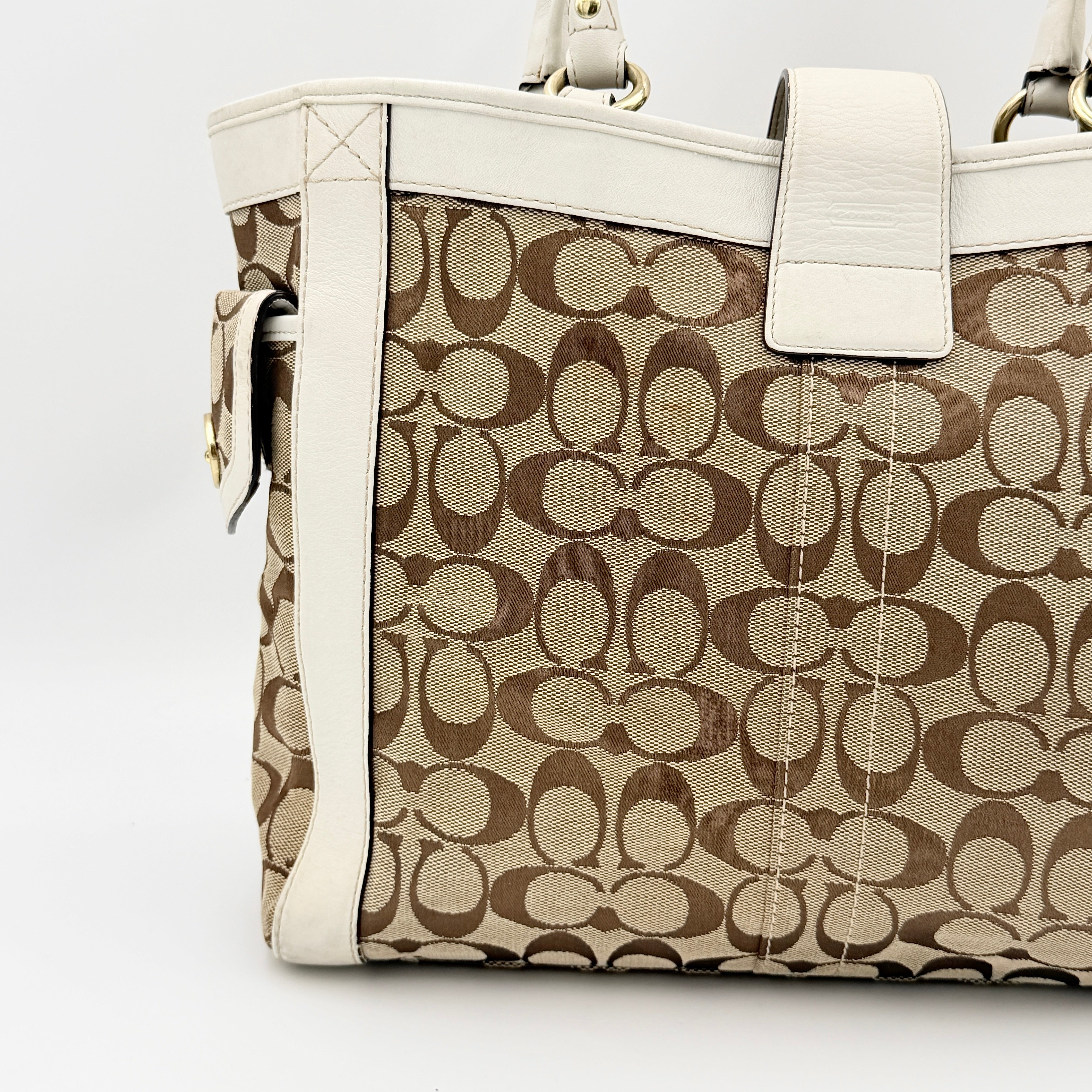 Coach Signature Soho Buckle Tote in beige canvas with white leather trim and gold-tone hardware, displayed against a clean background.