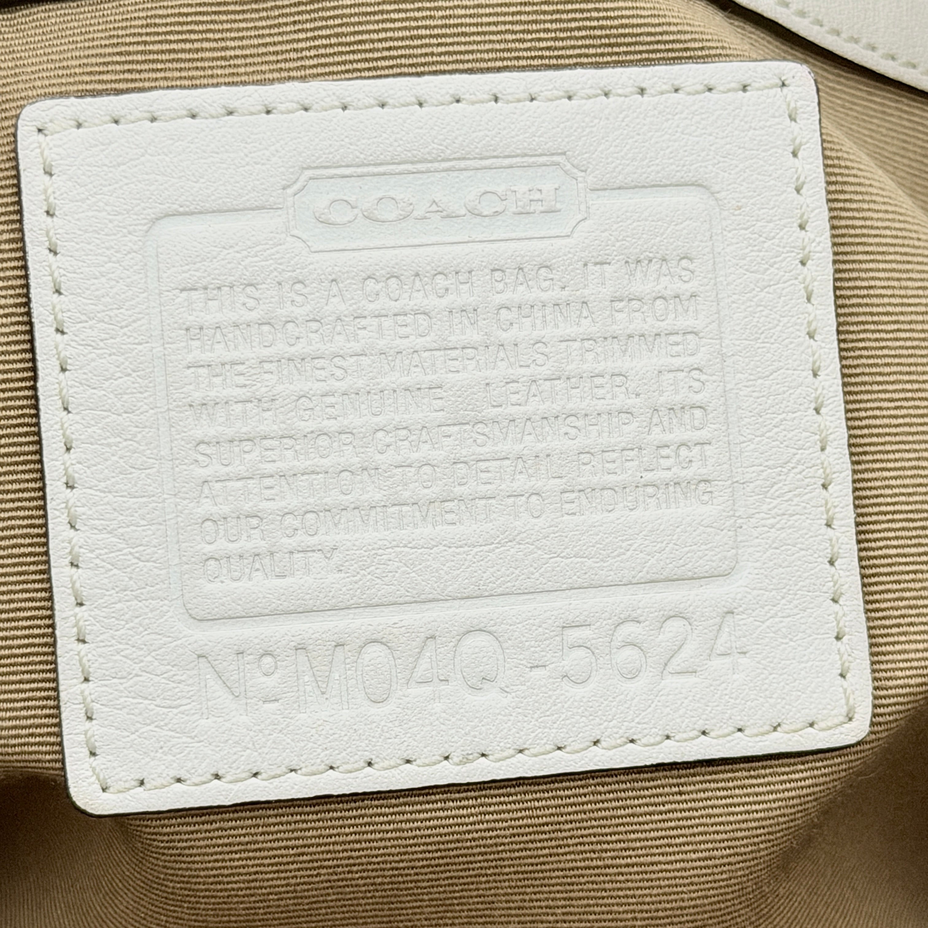 Coach Signature Soho Buckle Tote in beige canvas with white leather trim and gold-tone hardware, displayed against a clean background.