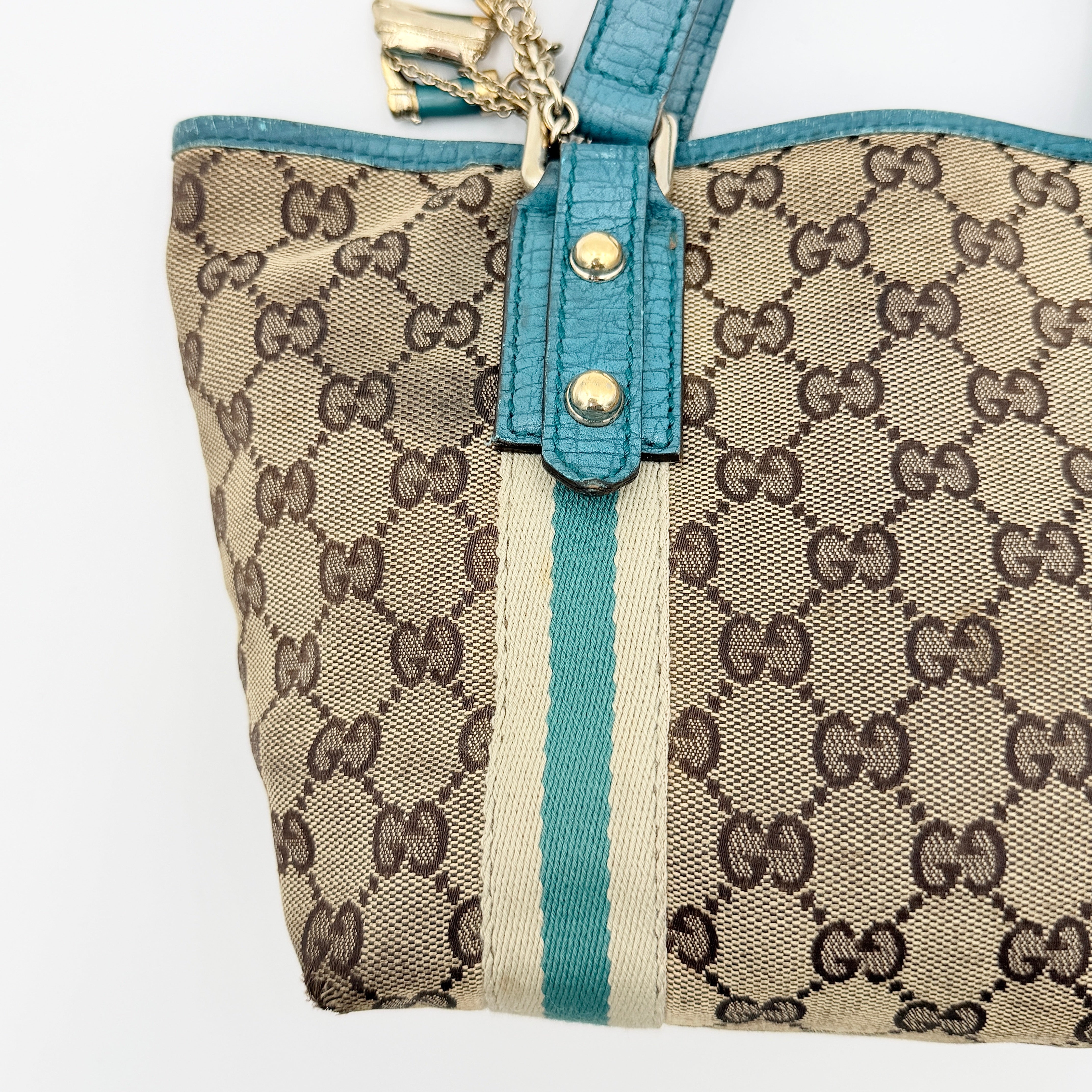 Gucci GG Monogram Jolicoeur Mini Shoulder Bag in beige canvas with teal blue leather trim and gold hardware, shown with a playful charm.