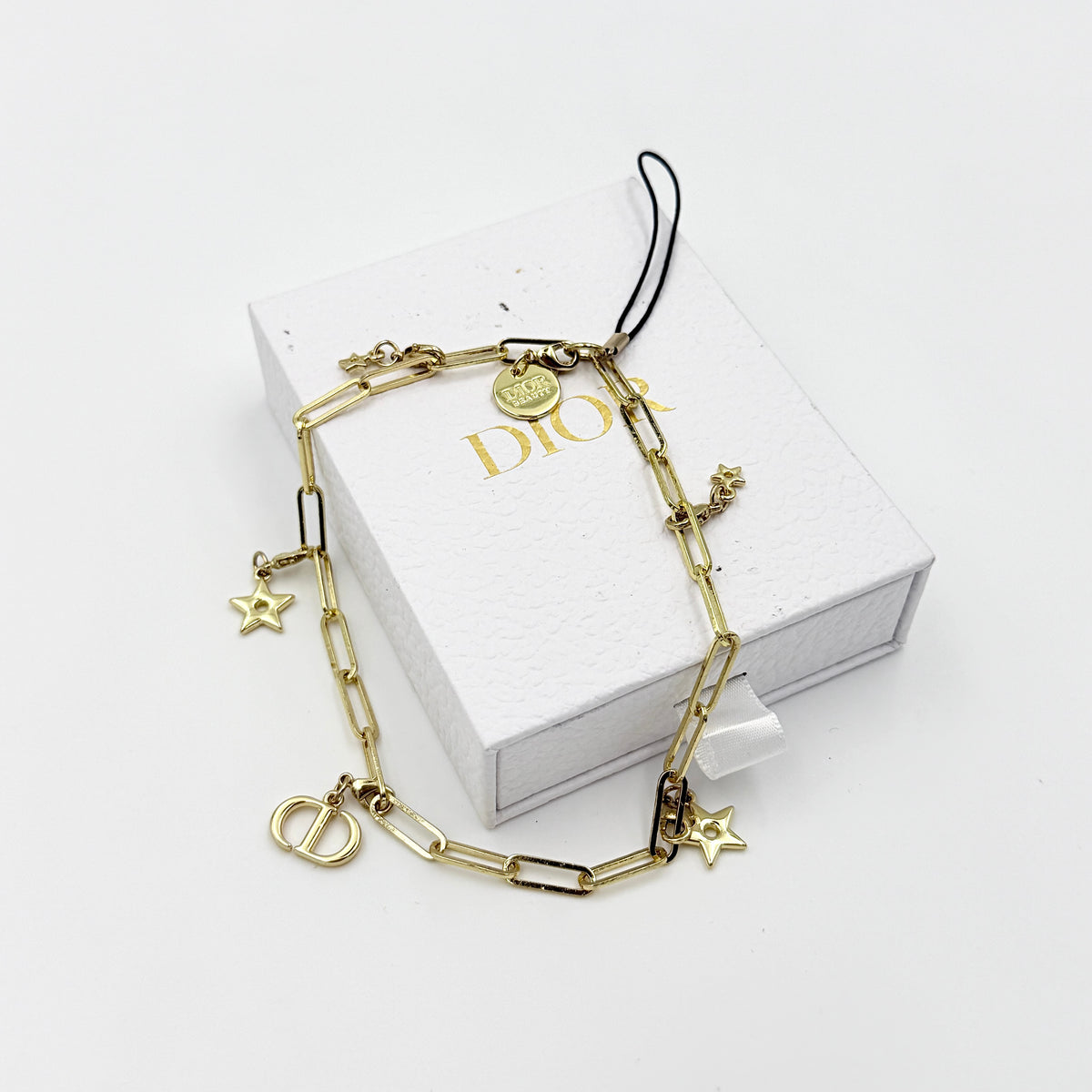 Christian Dior gold-tone phone strap with CD logo and star charms, styled with original Dior box.