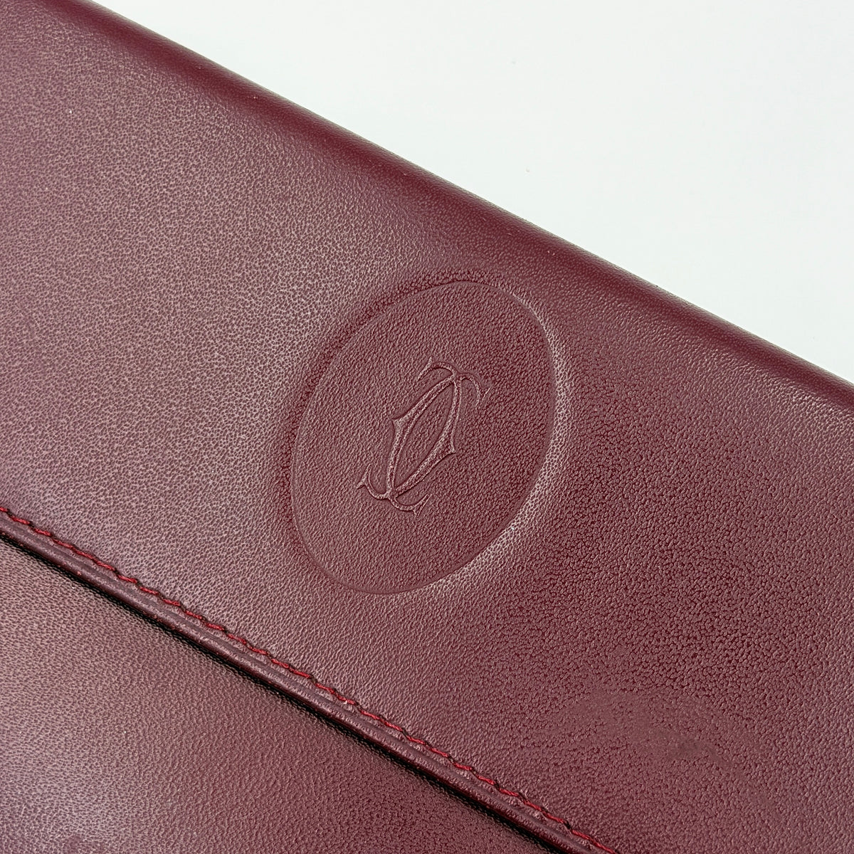 Cartier Must de Cartier trifold wallet in burgundy leather with gold-tone corners, showing the embossed double C logo on the front flap.
