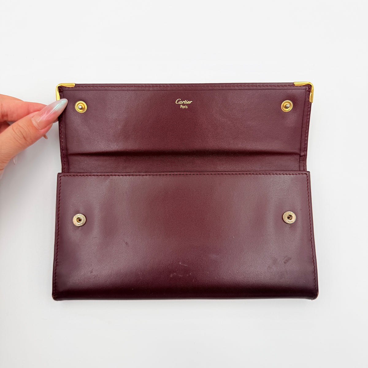 Cartier Must de Cartier trifold wallet in burgundy leather with gold-tone corners, showing the embossed double C logo on the front flap.