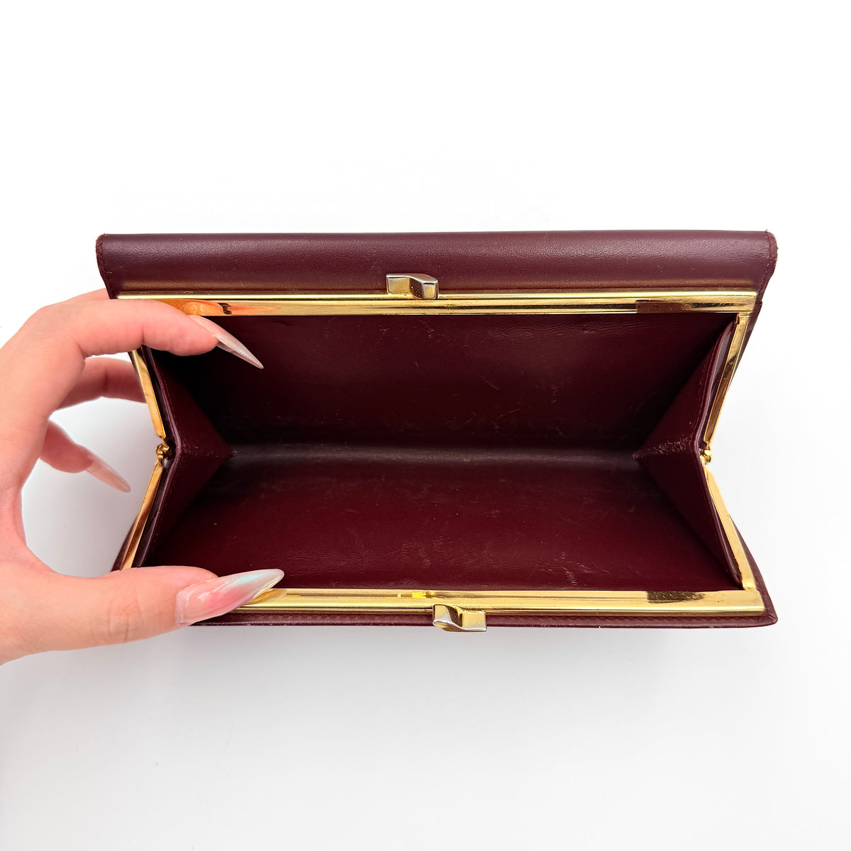 Cartier Must de Cartier trifold wallet in burgundy leather with gold-tone corners, showing the embossed double C logo on the front flap.