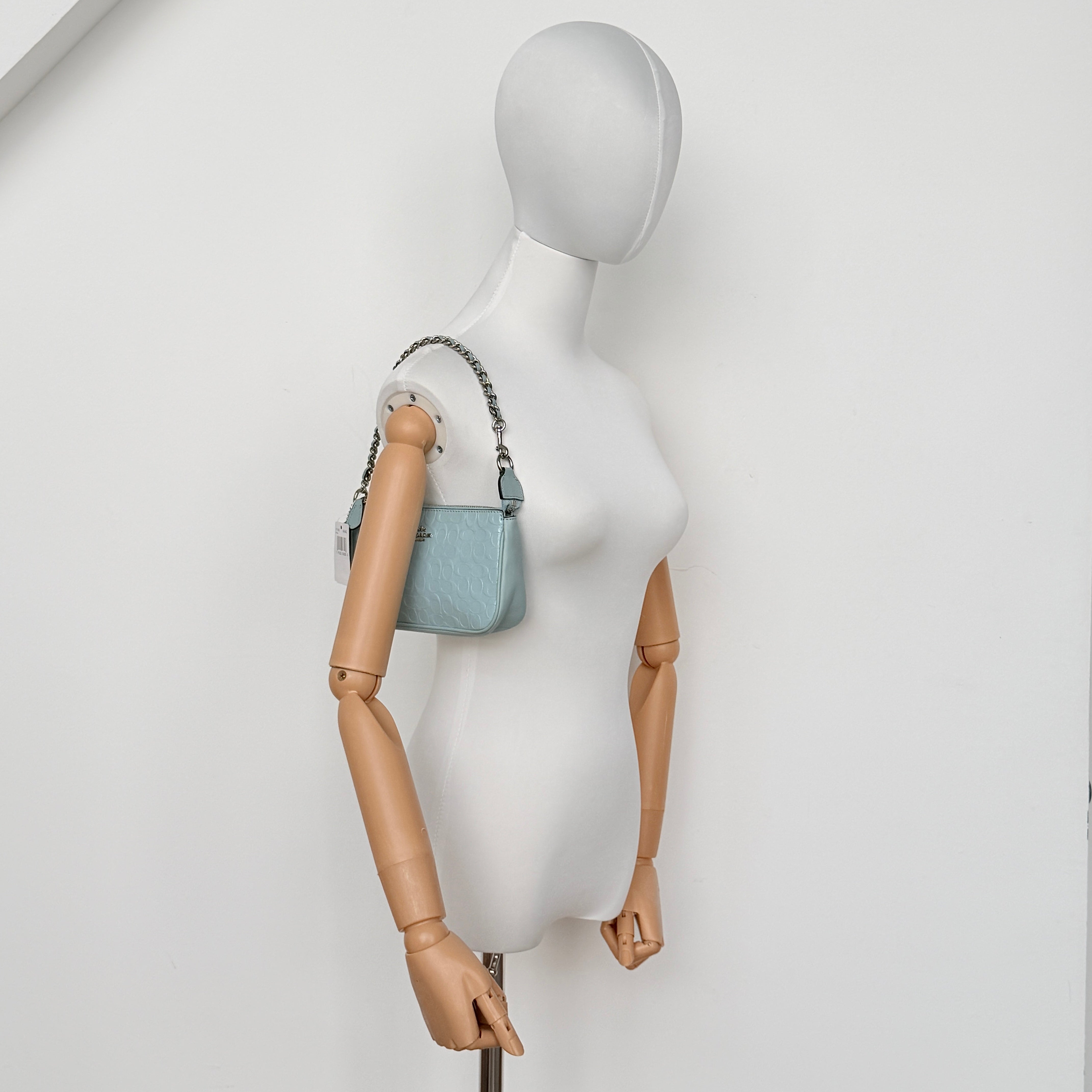 Coach Nolita 19 small shoulder bag in light blue embossed patent leather with silver-tone chain strap shown against a white background.