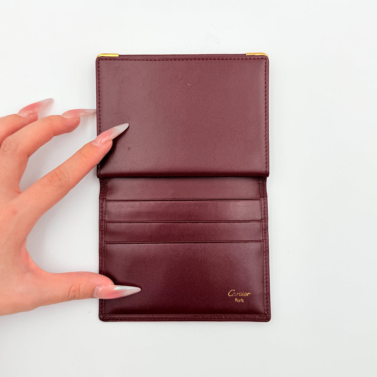Cartier Must de Cartier card case in rich burgundy leather with gold-tone corner details and an embossed logo.