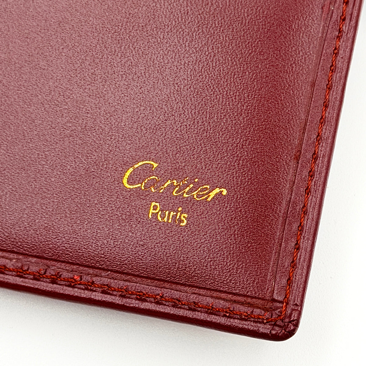 Cartier Must de Cartier card case in rich burgundy leather with gold-tone corner details and an embossed logo.