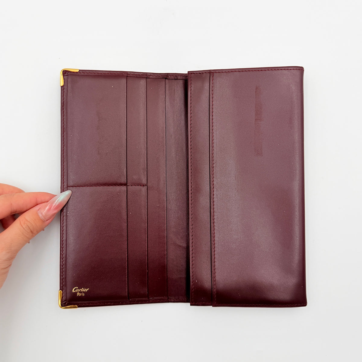 Cartier Must de Cartier bifold long wallet in burgundy leather with gold-tone corners.