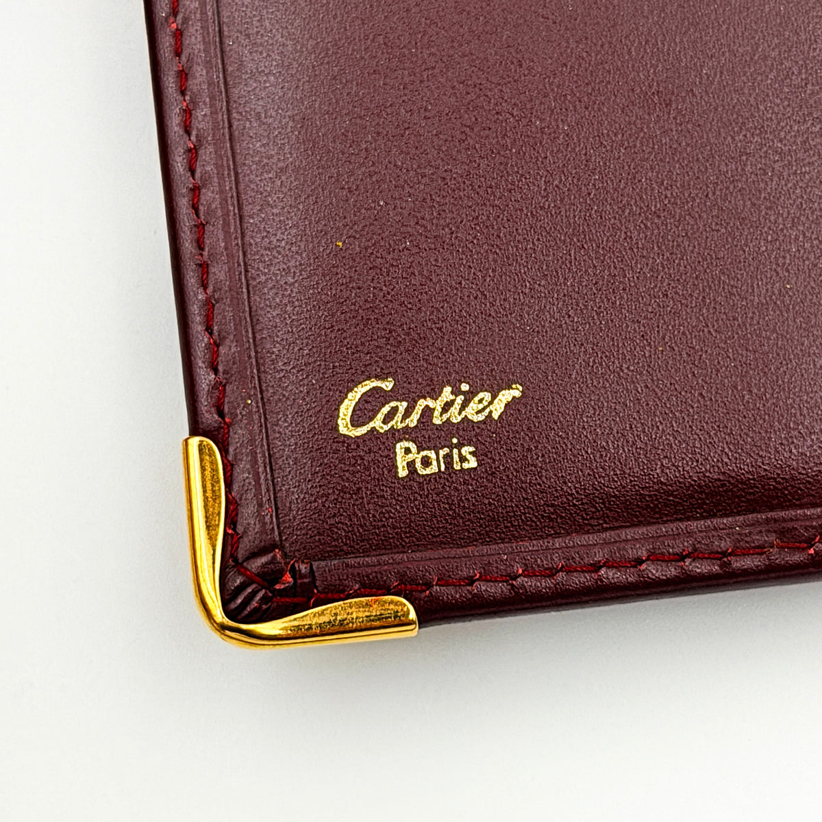 Cartier Must de Cartier bifold long wallet in burgundy leather with gold-tone corners.