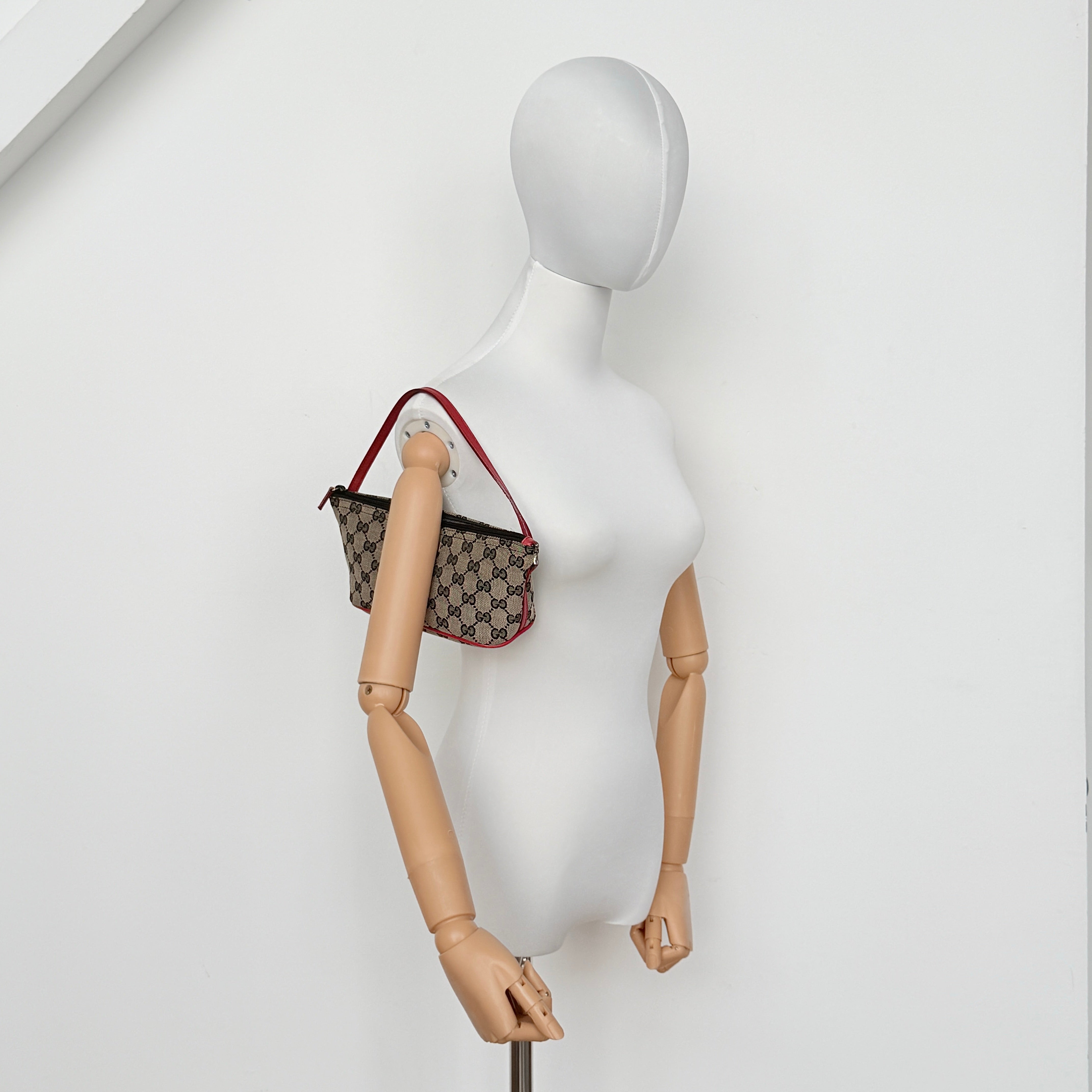 Gucci GG Monogram Pochette Boat Shoulder Bag in grey canvas with red leather trim and gold plaque, shown against a plain background.