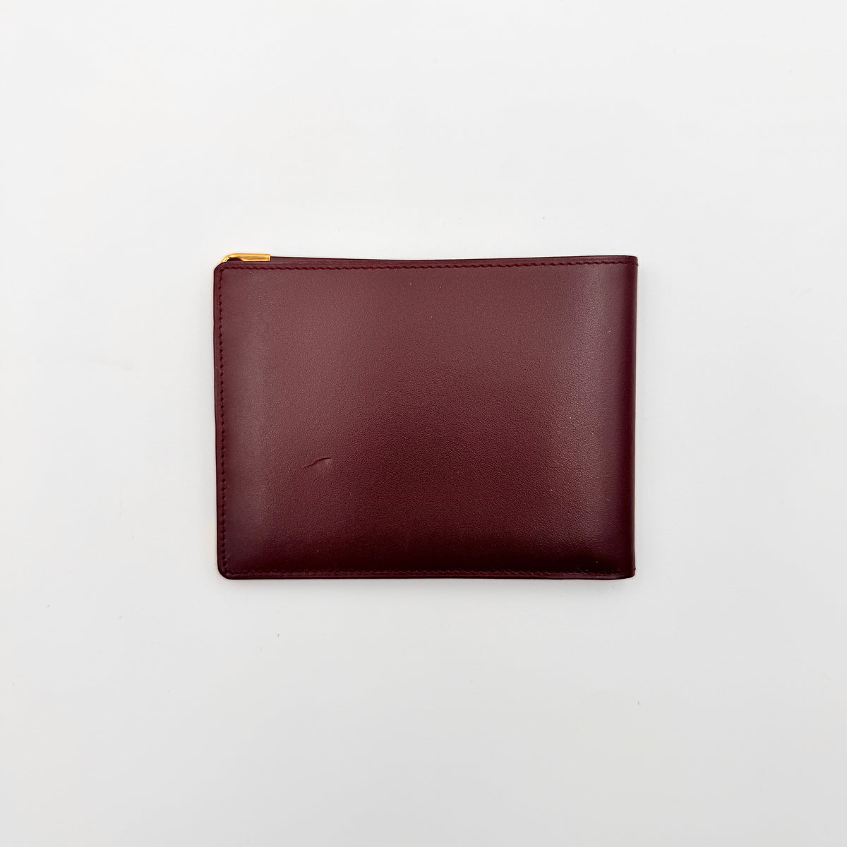 Cartier Must de Cartier burgundy leather bifold wallet with gold-tone corner accents shown against a white background.