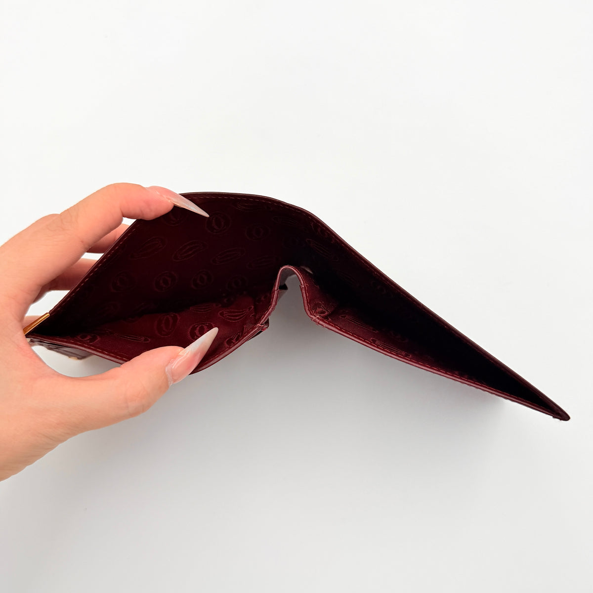 Cartier Must de Cartier burgundy leather bifold wallet with gold-tone corner accents shown against a white background.