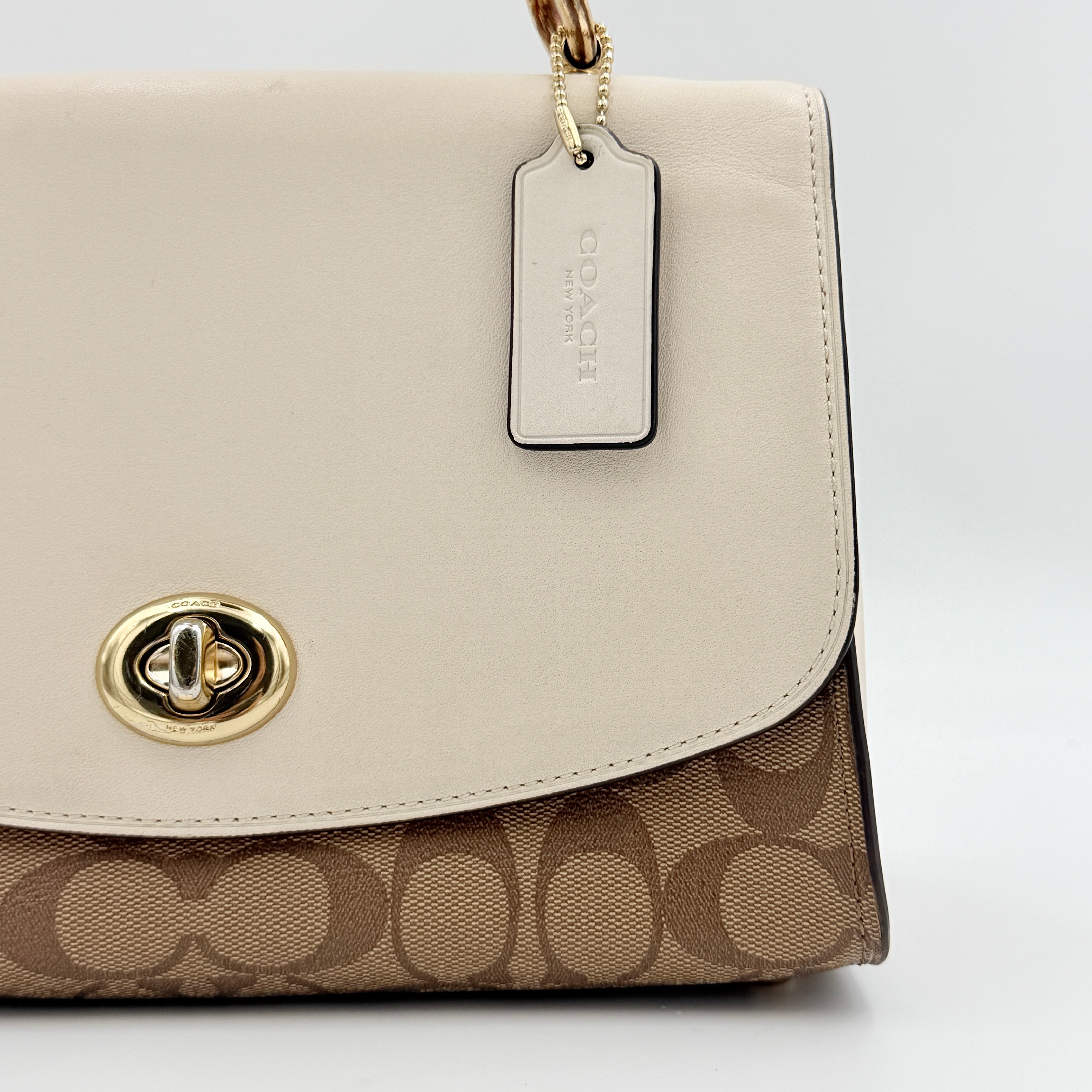 Coach Signature Tilly Top Handle Bag in beige and white with gold-tone hardware and detachable strap, displayed against a clean background.