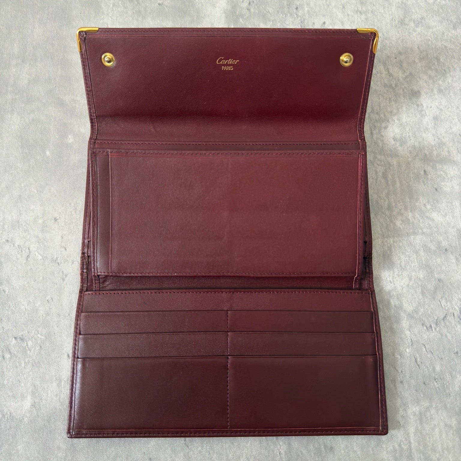Cartier Must de Cartier trifold continental wallet in burgundy leather, showcasing detailed craftsmanship, gold-tone Cartier logo, and an organized interior.