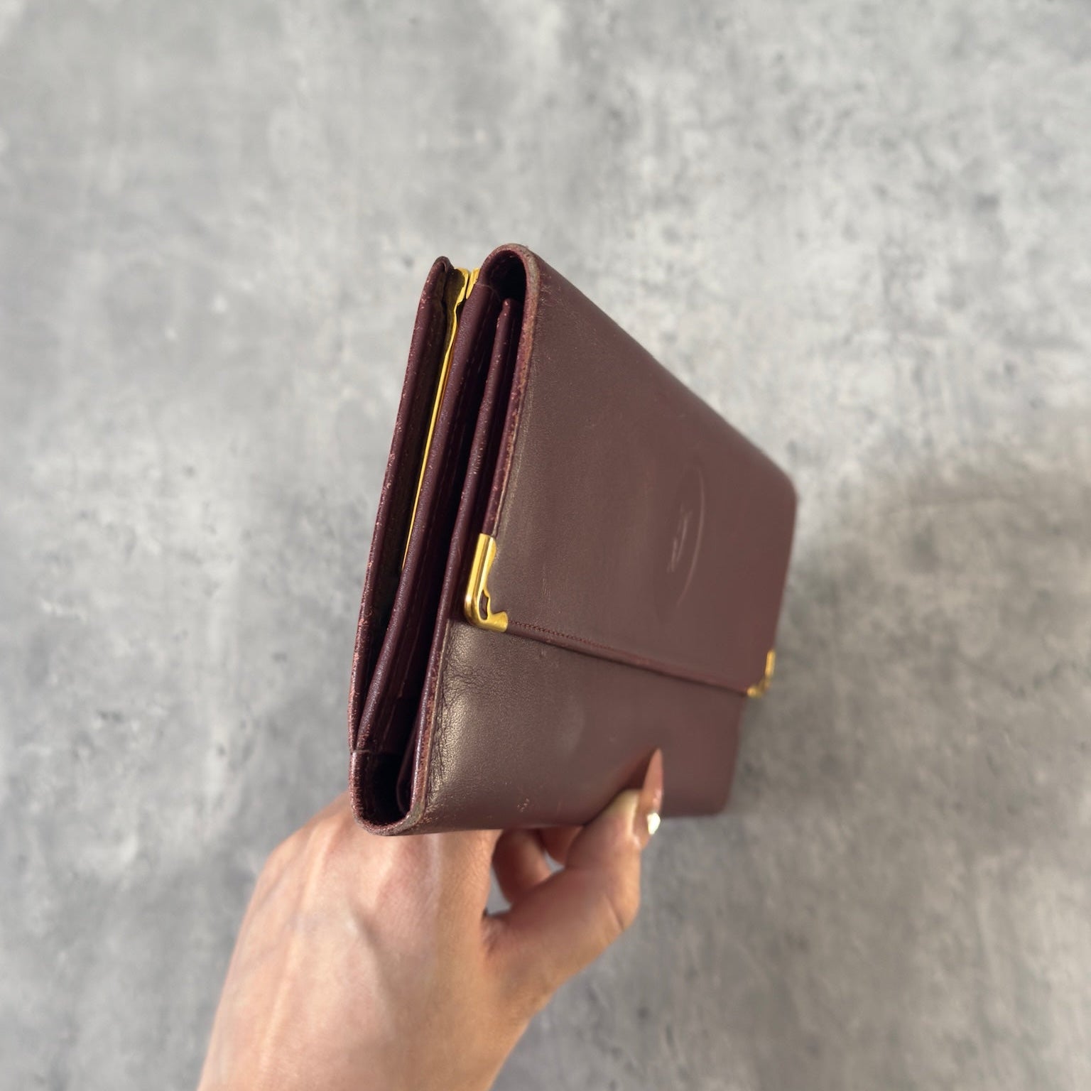 Cartier Must de Cartier trifold continental wallet in burgundy leather, showcasing detailed craftsmanship, gold-tone Cartier logo, and an organized interior.