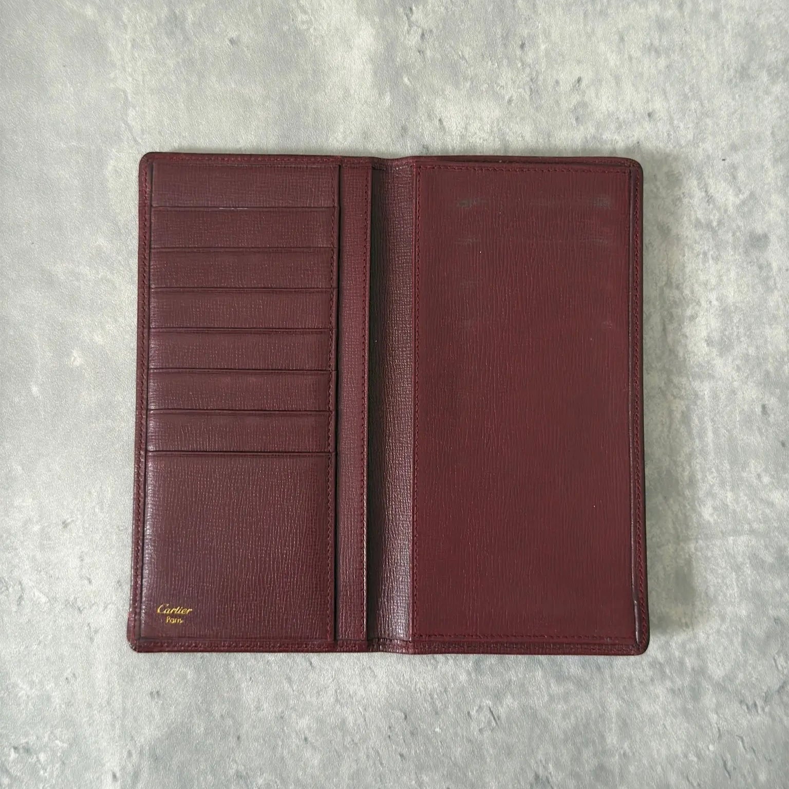 Cartier Must de Cartier Bifold Long Wallet in rich burgundy leather, detailed with multiple card slots, bill compartments, and a discreet embossed logo on the front cover.