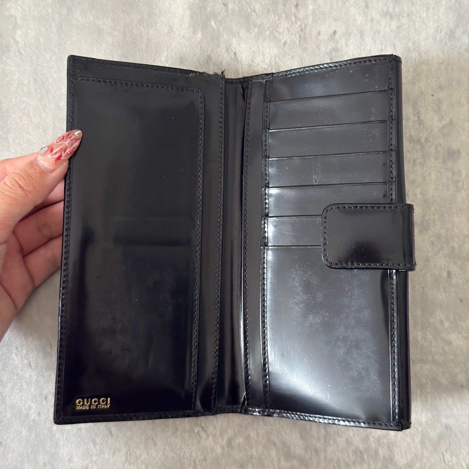 Gucci Continental Wallet in black patent leather, featuring a gold-tone Gucci logo, multiple card slots, and a spacious interior, epitomizes luxury and functionality.