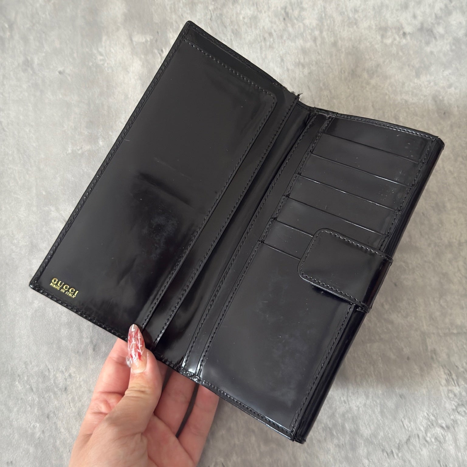 Gucci Continental Wallet in black patent leather, featuring a gold-tone Gucci logo, multiple card slots, and a spacious interior, epitomizes luxury and functionality.