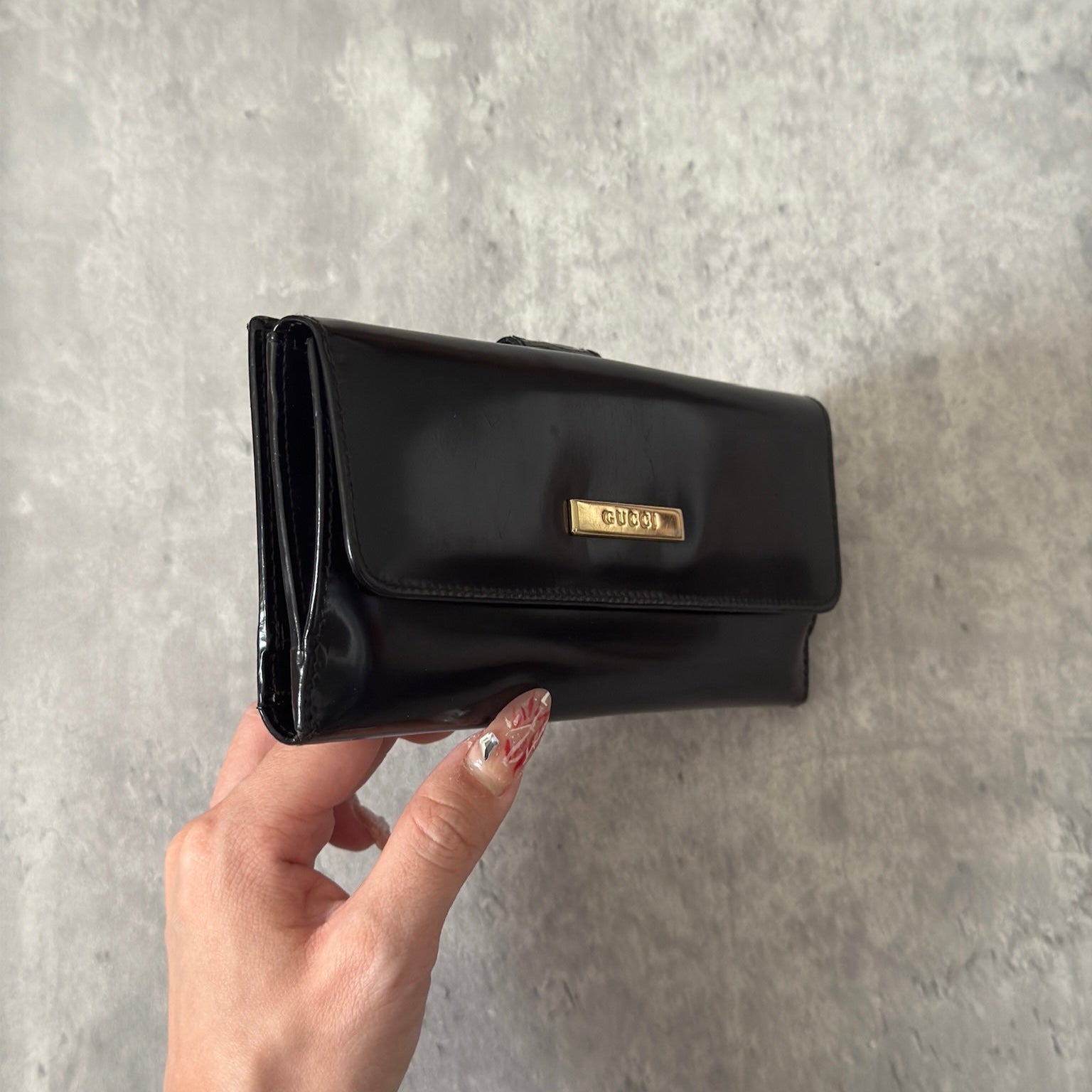Gucci Continental Wallet in black patent leather, featuring a gold-tone Gucci logo, multiple card slots, and a spacious interior, epitomizes luxury and functionality.