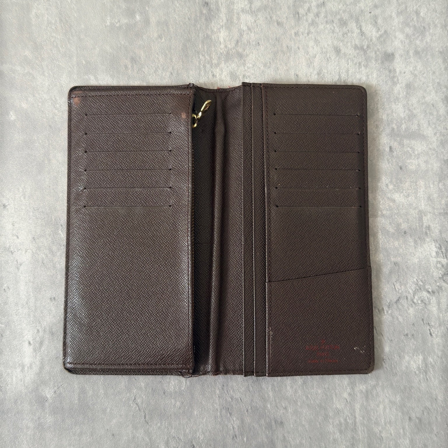 Louis Vuitton Damier Ebene Brazza wallet in dark brown and black checkered canvas, featuring a snap closure and organized interior with card slots and bill compartments.