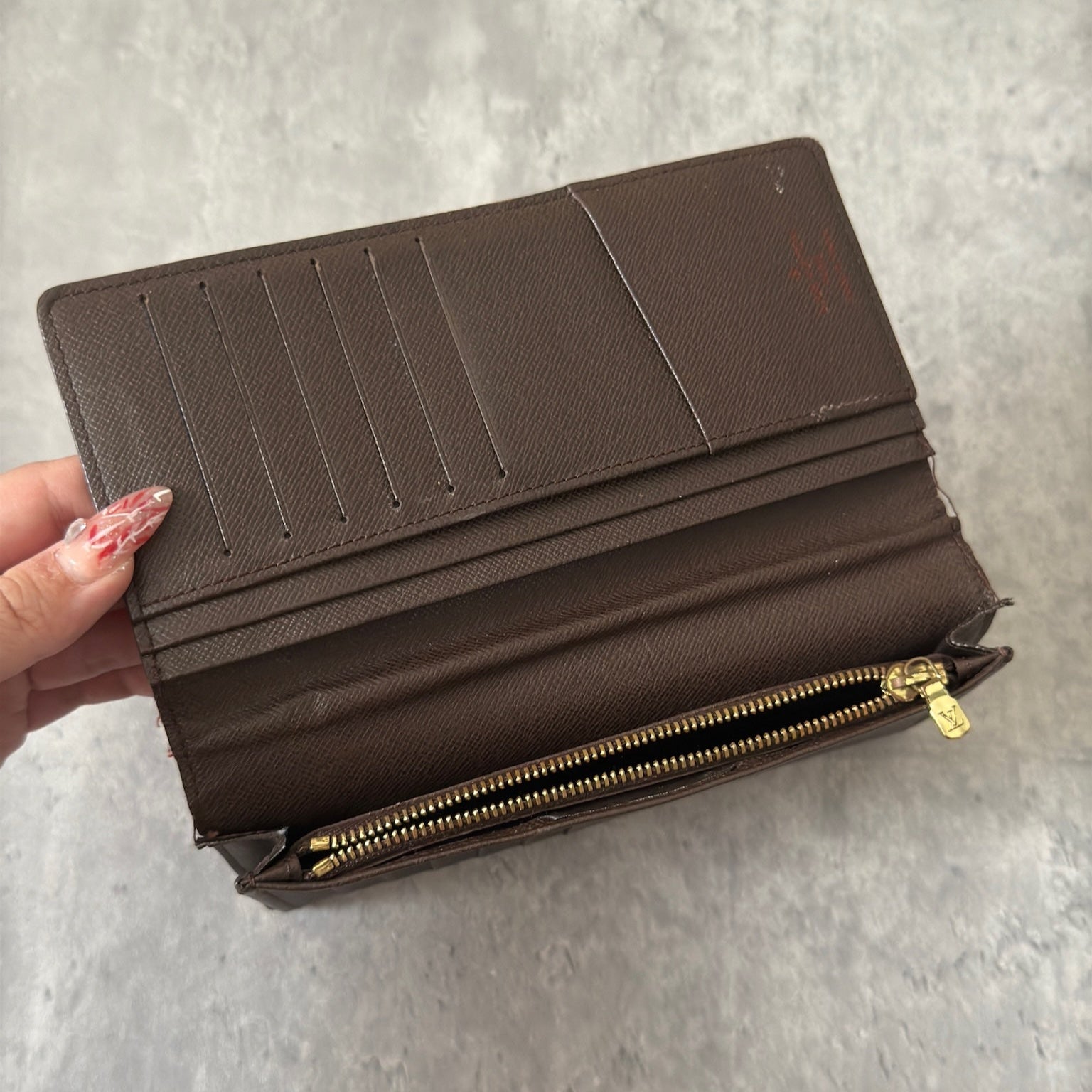 Louis Vuitton Damier Ebene Brazza wallet in dark brown and black checkered canvas, featuring a snap closure and organized interior with card slots and bill compartments.