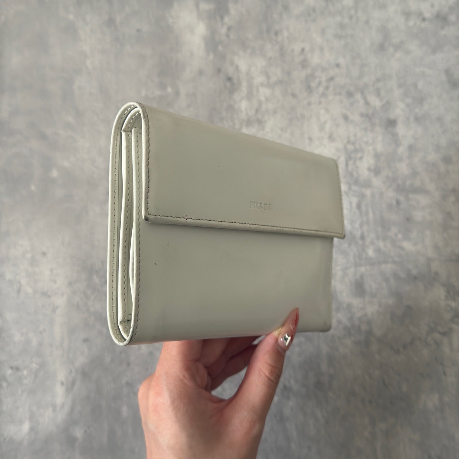 Prada City Calf Leather Compact Wallet in off-white with flap closure and embossed logo detail, showcasing a sophisticated, minimalist design.