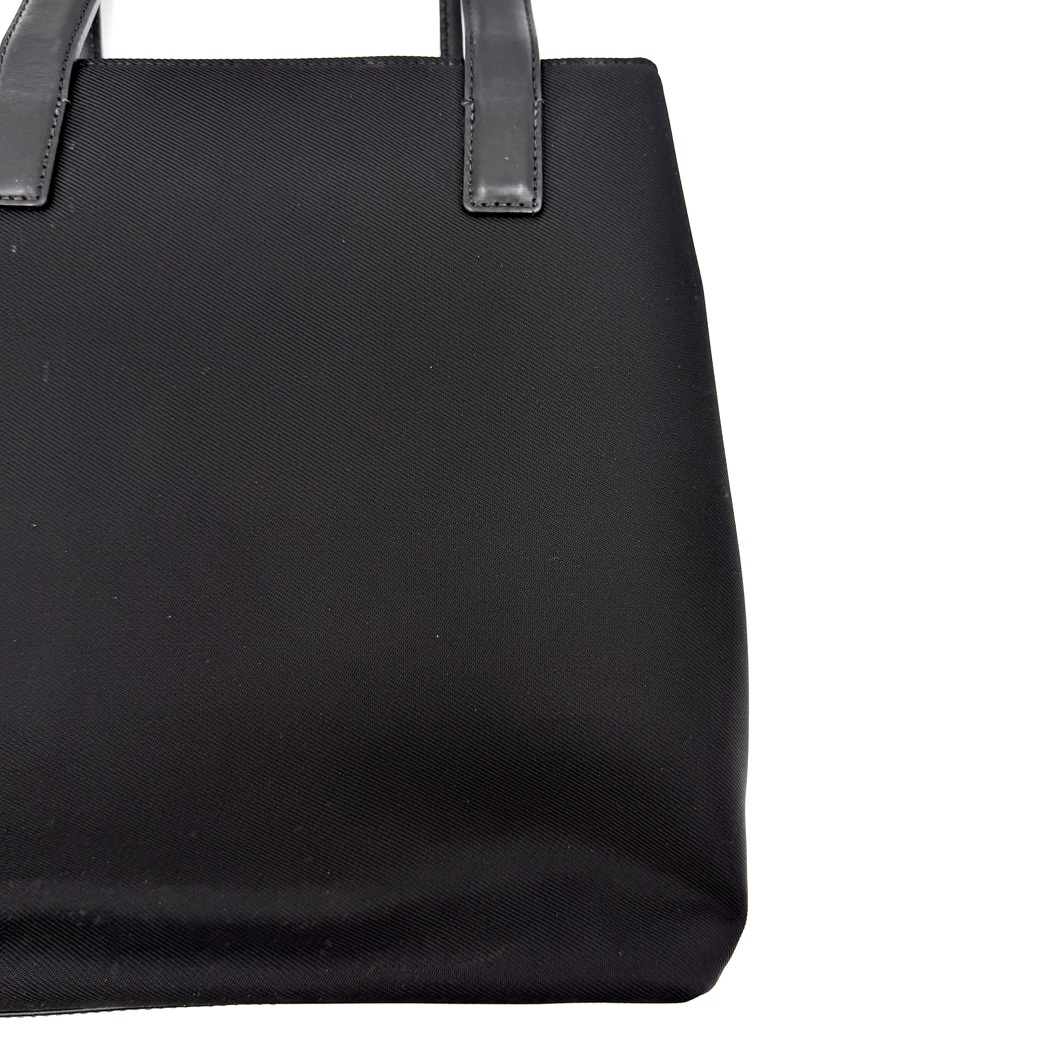 Coach Mercer Nylon Tote Bag in black with structured silhouette, leather handles, and subtle silver logo plaque at the base.