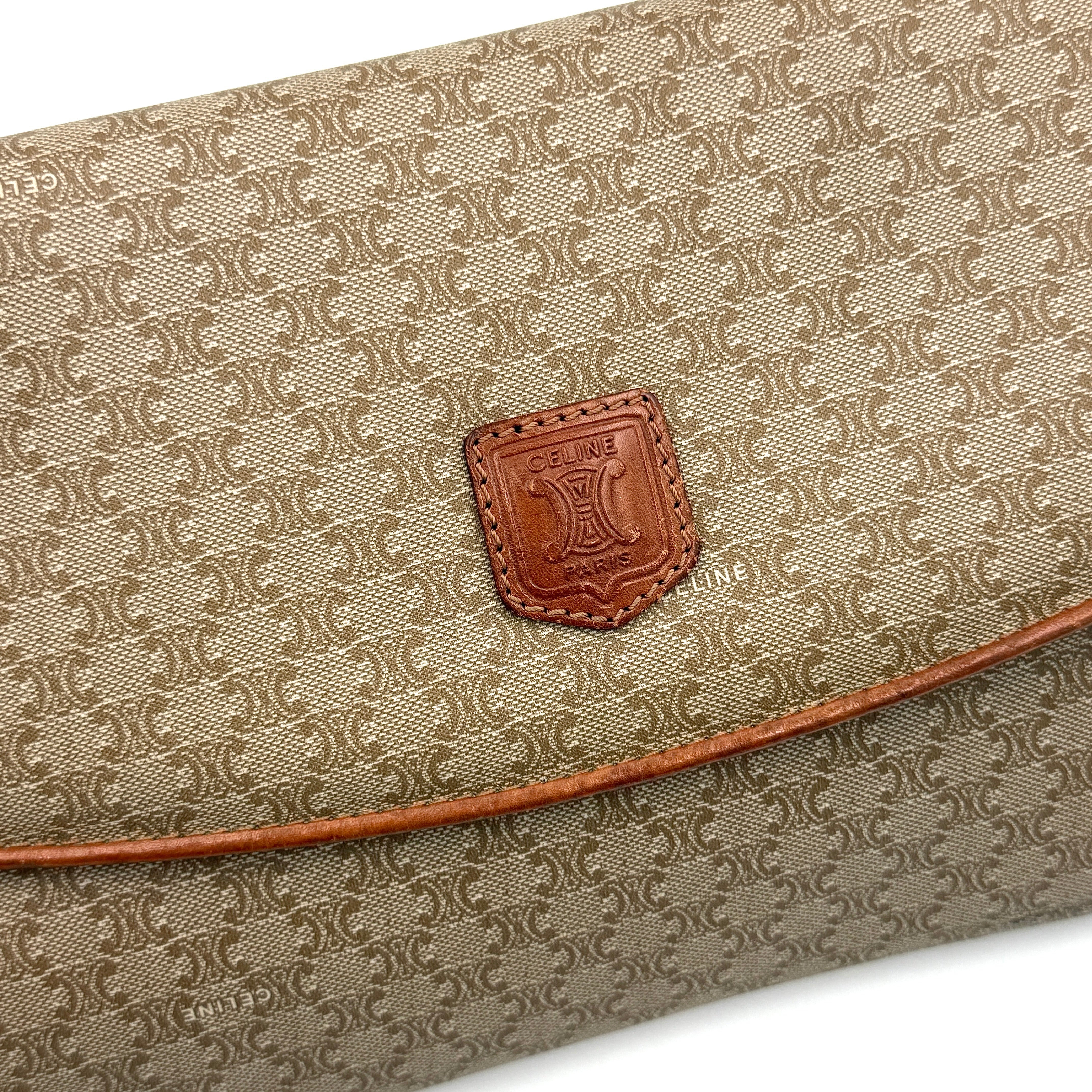 The Celine Macadam Clutch Bag in beige, featuring the iconic monogram canvas and tan leather trim, shown neatly closed with its signature emblem on the flap.