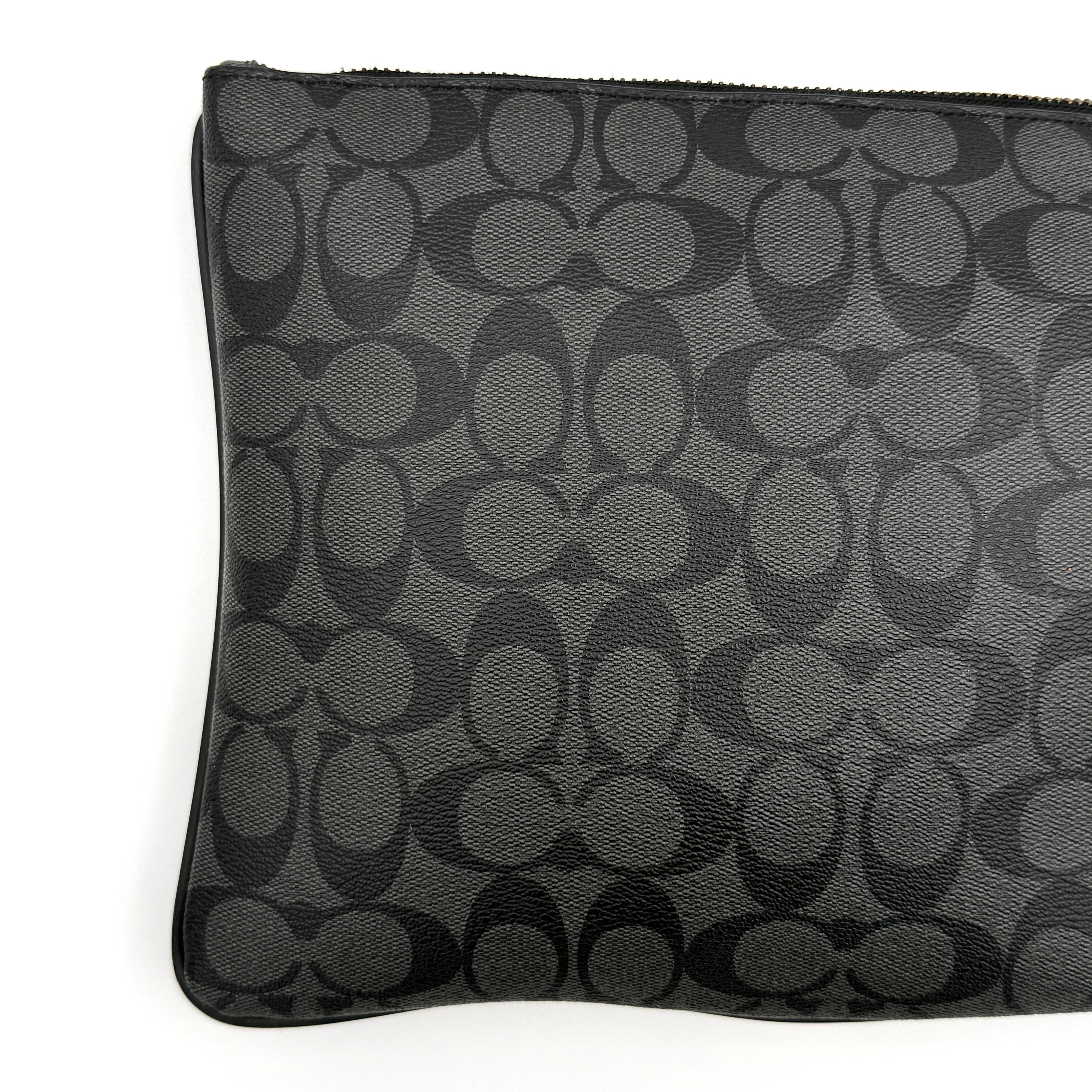 Coach Signature large pouch in black coated canvas with navy and cream varsity stripes, shown from the front with a zip top.