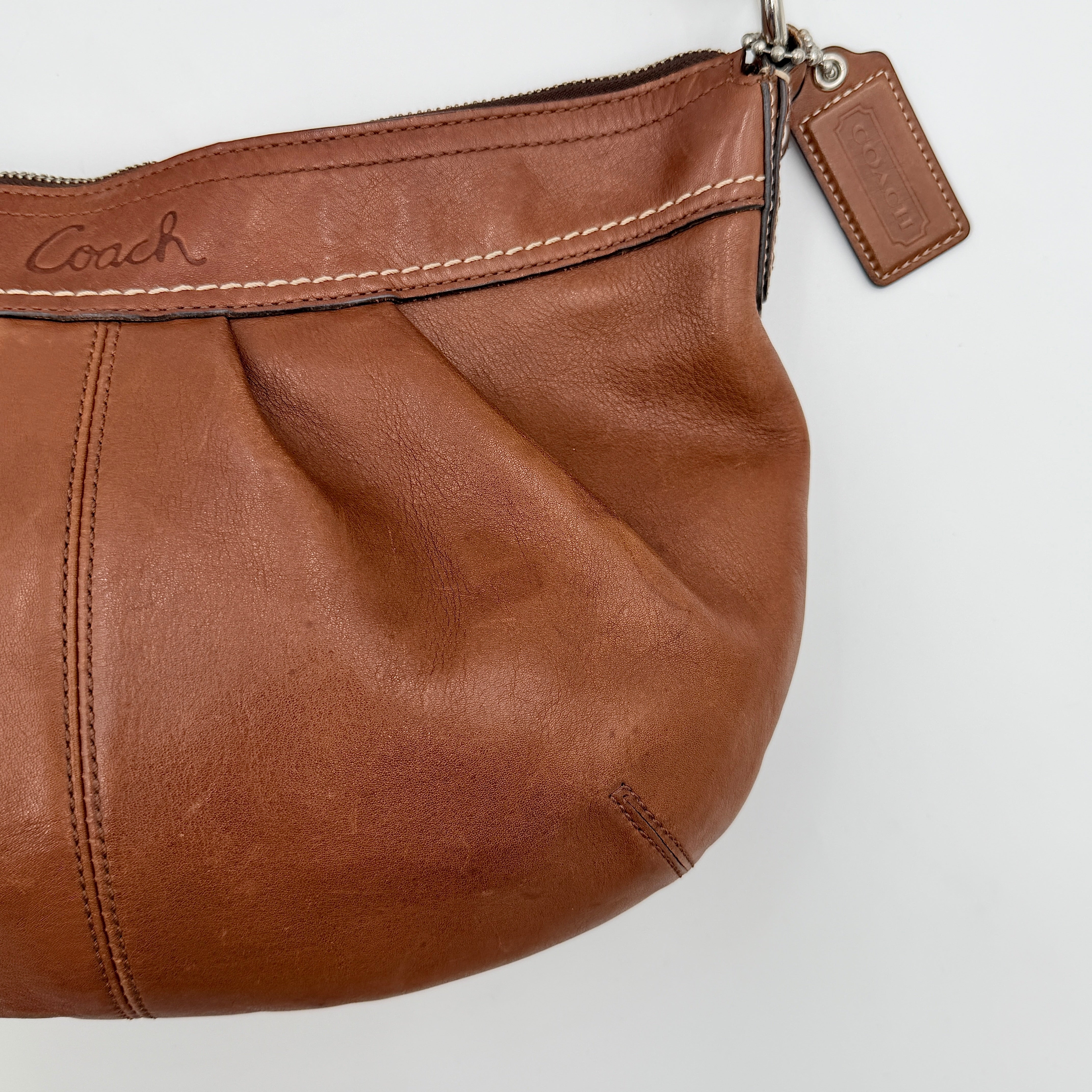 Coach Soho Hobo brown leather shoulder bag with pleated detailing and silver hardware, shown on a white background.