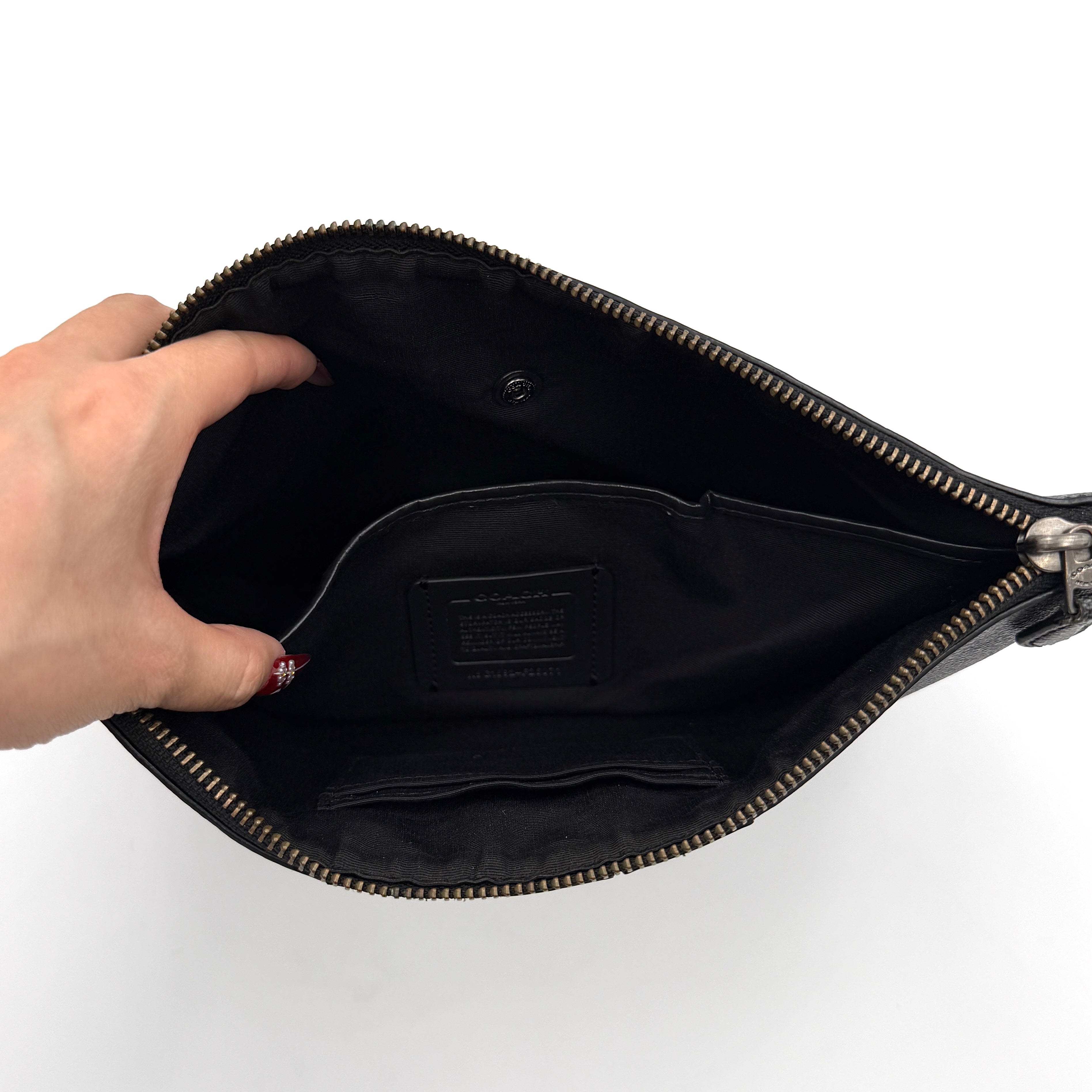 Coach Signature large pouch in black coated canvas with navy and cream varsity stripes, shown from the front with a zip top.