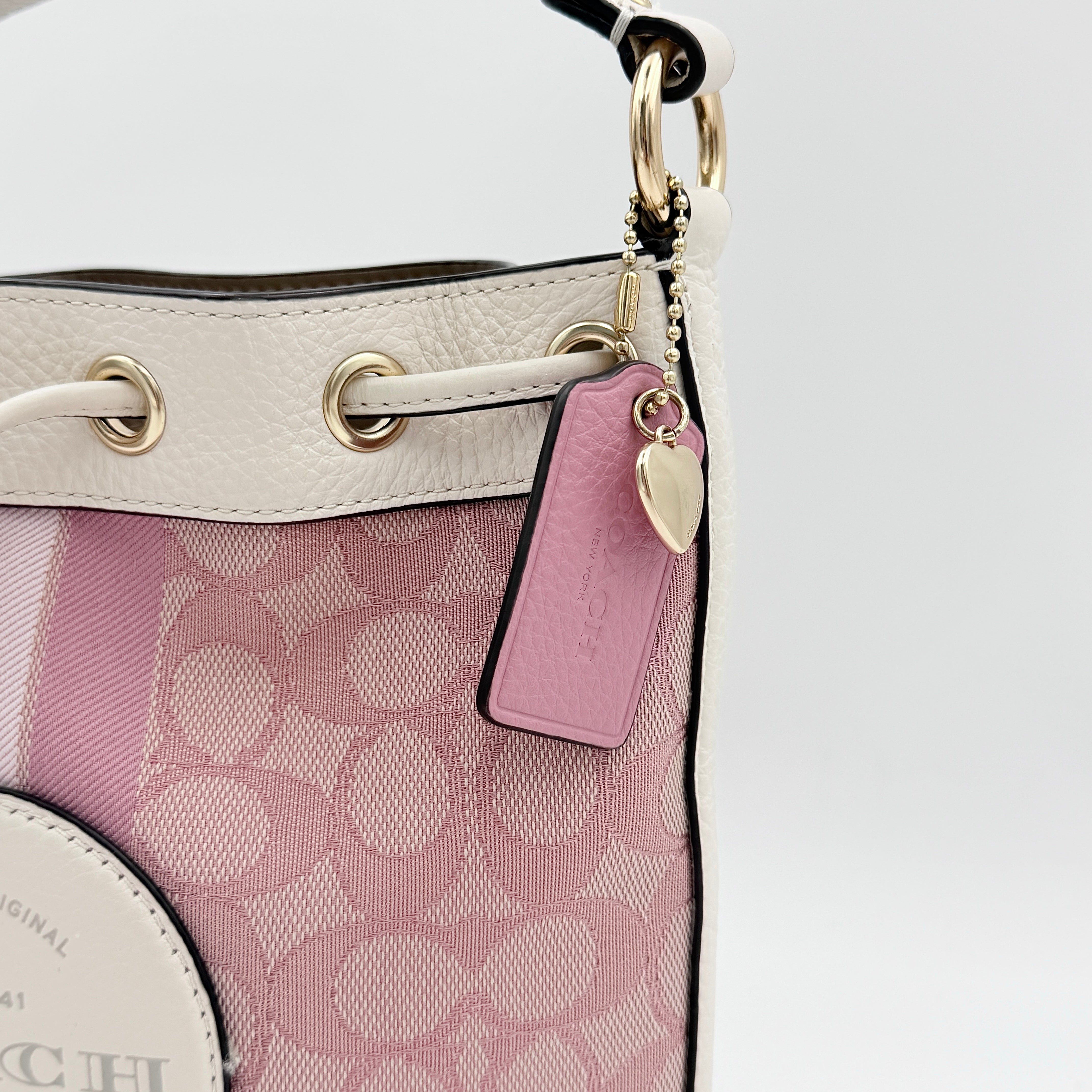 Coach Signature Dempsey 19 bucket bag in pink and white canvas with white leather trim and detachable strap.
