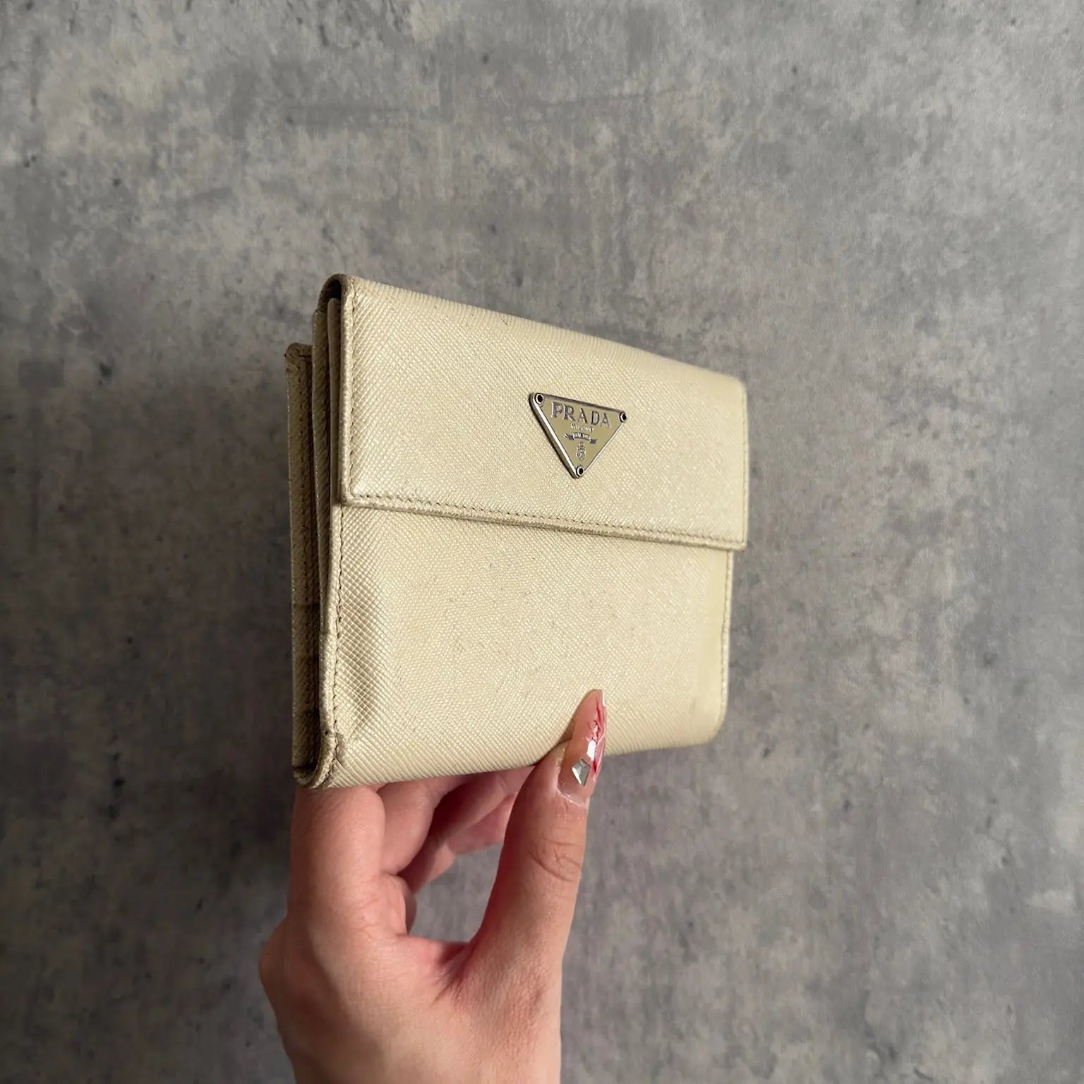 Prada Cream Saffiano Folding Leather Wallet, crafted from textured Saffiano leather with a gold-tone triangular logo and a compact folding design.