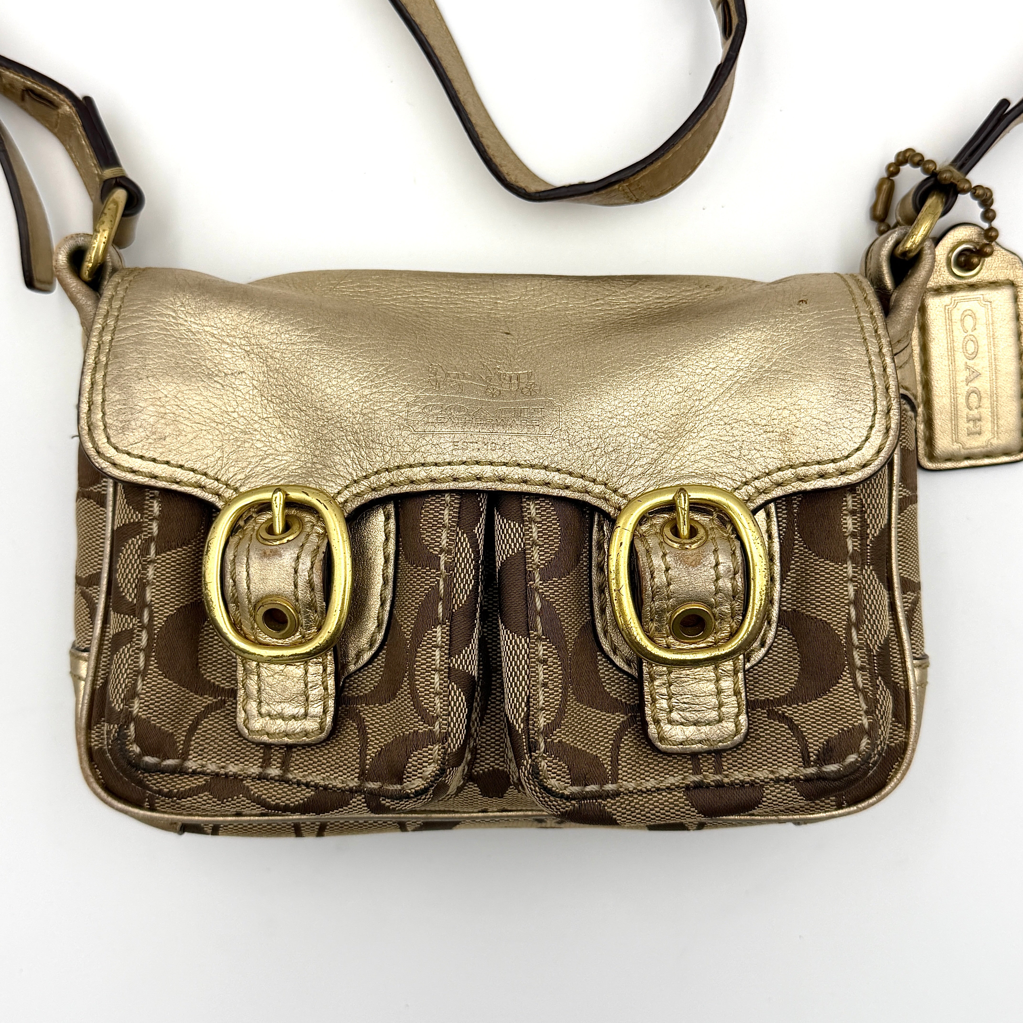 Coach Bleecker crossbody bag in gold metallic leather and beige monogram canvas with double front buckle details.