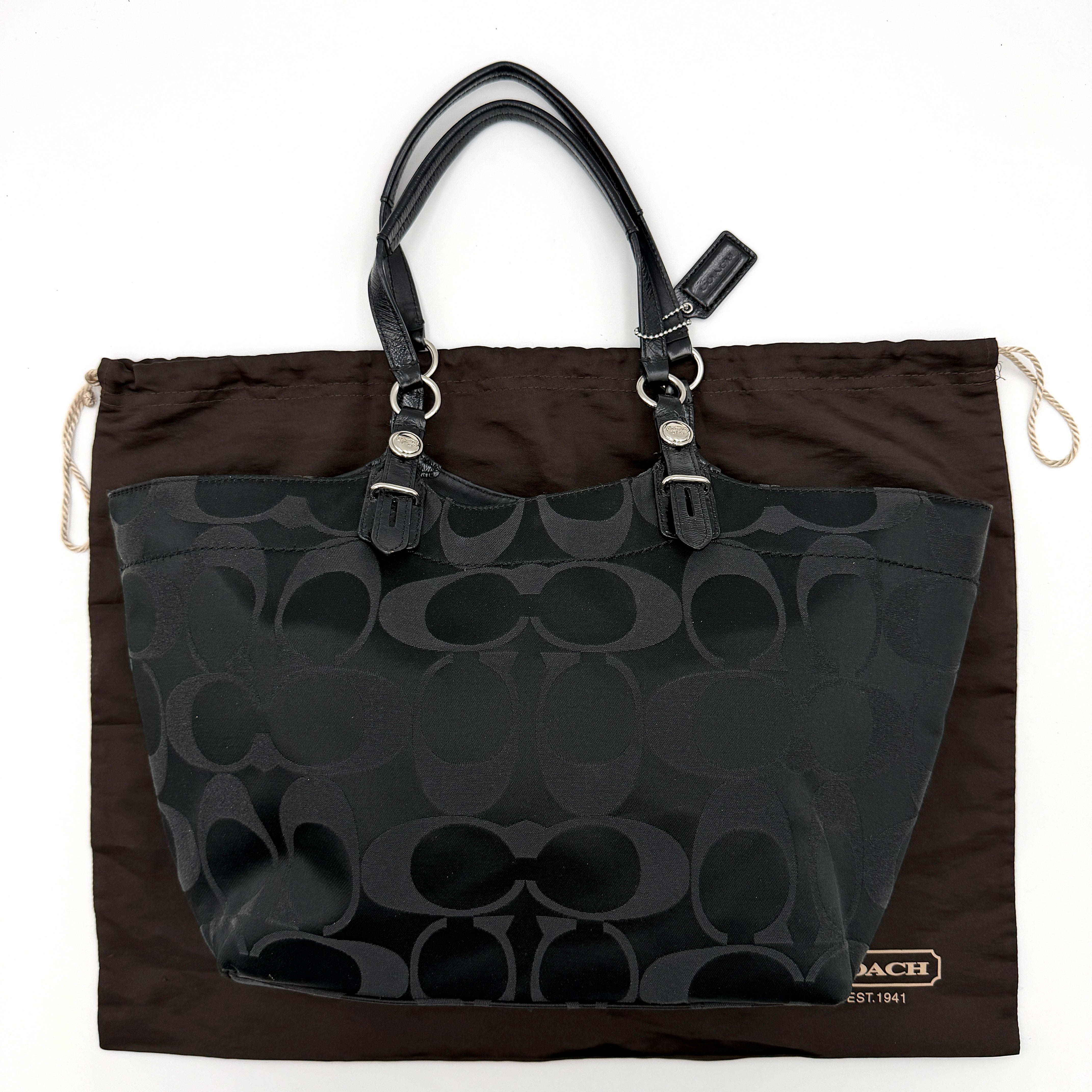 Coach black signature canvas tote with leather handles and silver hardware, set against a white background.
