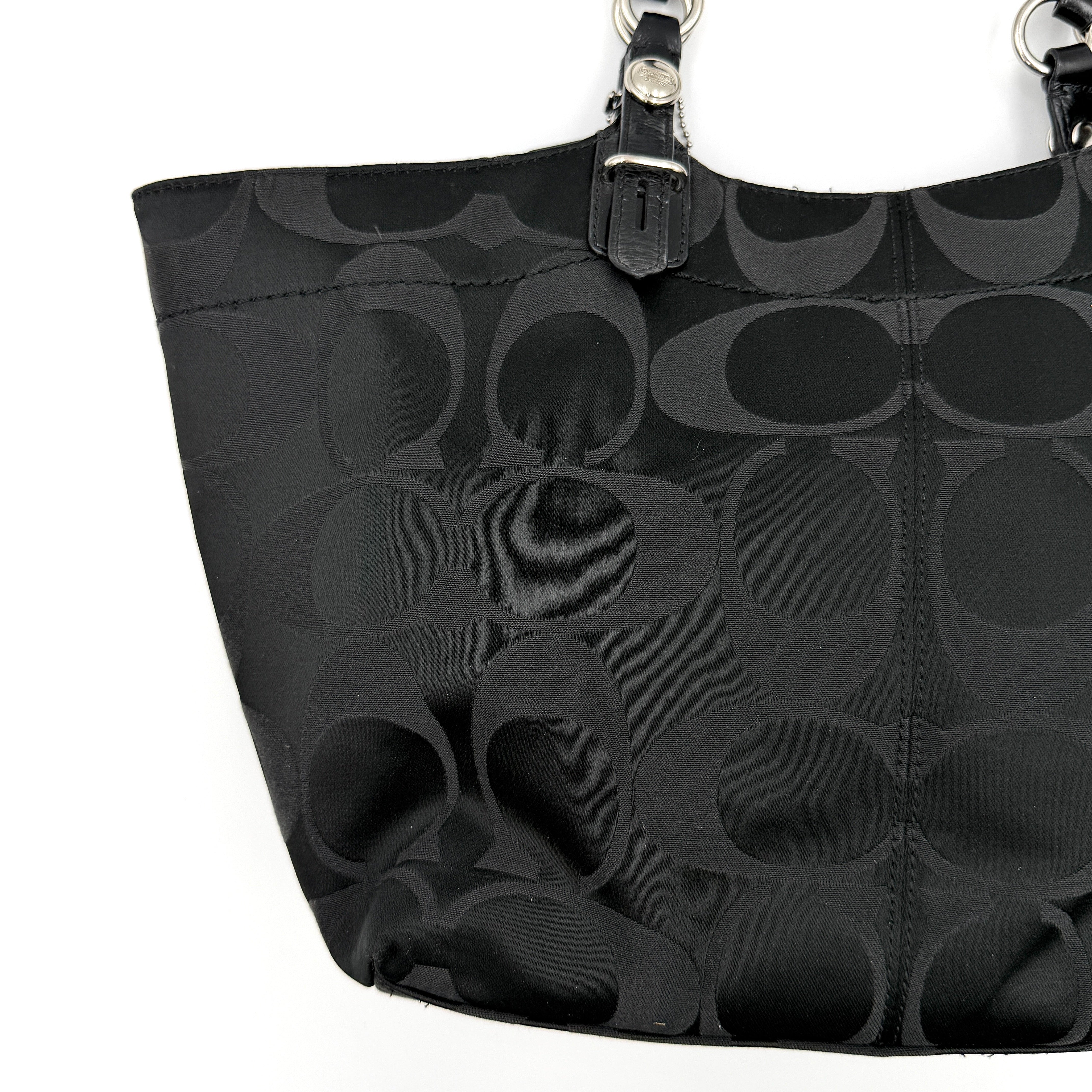 Coach black signature canvas tote with leather handles and silver hardware, set against a white background.