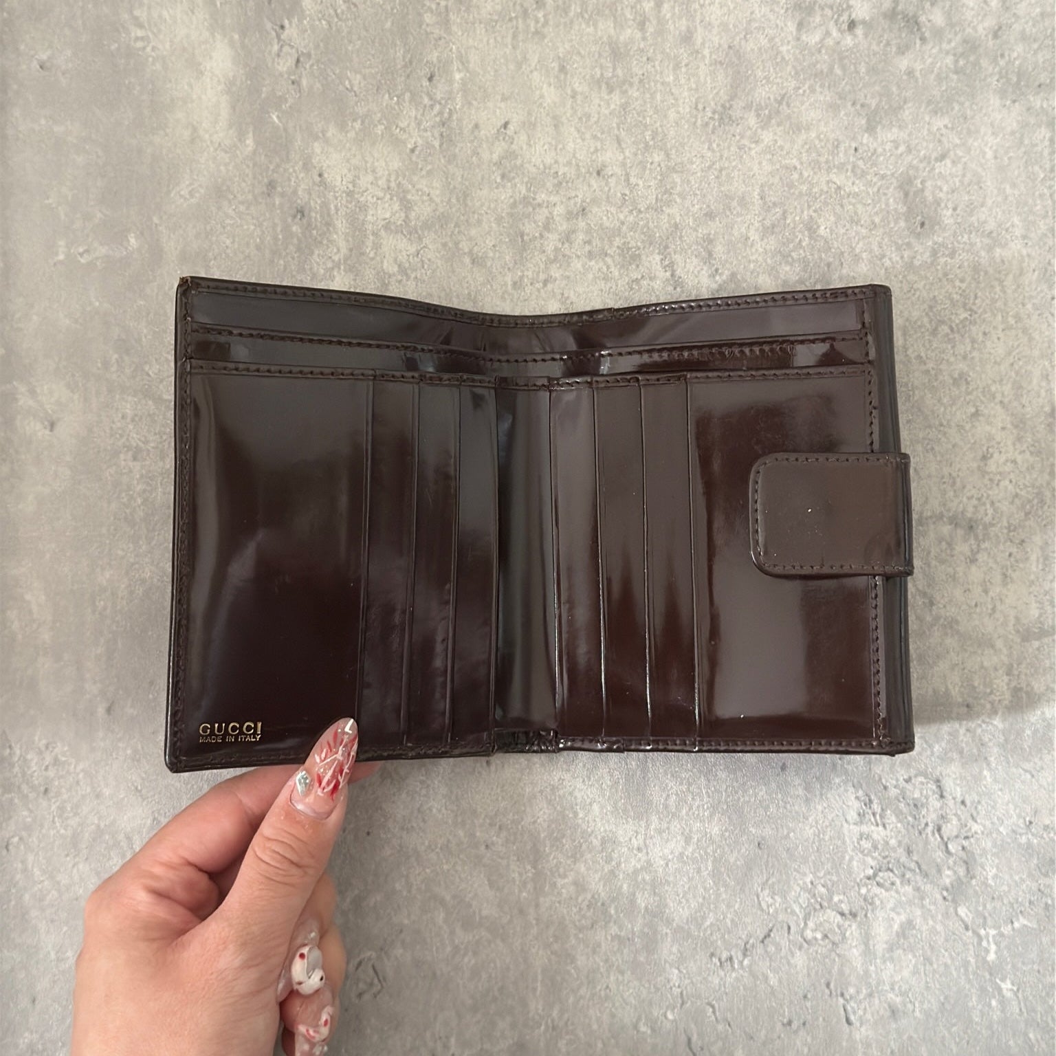Gucci brown patent leather bifold wallet with multiple card slots and bill compartments, showcasing classic style and luxury.