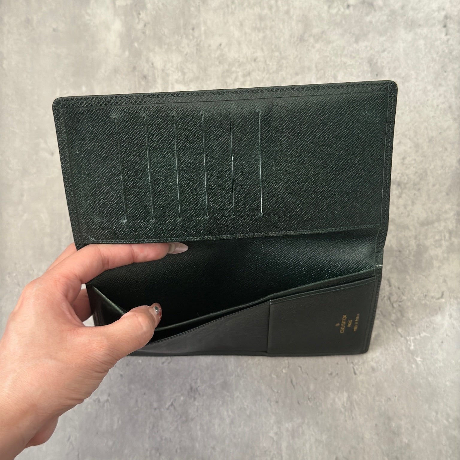 Louis Vuitton Taiga Porte-Valeurs long wallet in green, showcasing the embossed LV logo and a structured interior with multiple card slots and compartments, embodying luxury and organization.