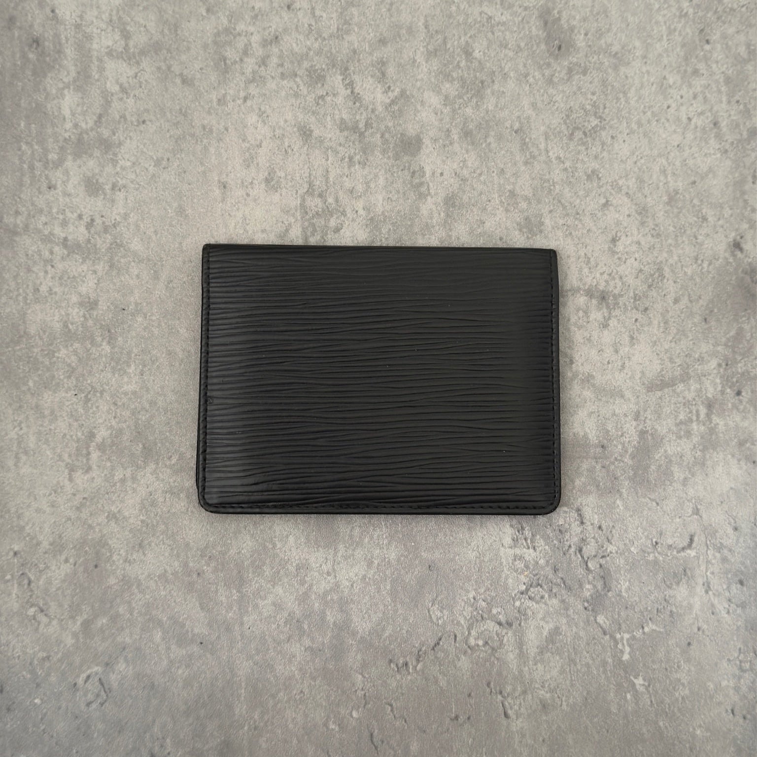 Luxurious black leather Louis Vuitton vintage card, ID, and passport holder featuring embossed logo, designed for sophisticated organization and style.