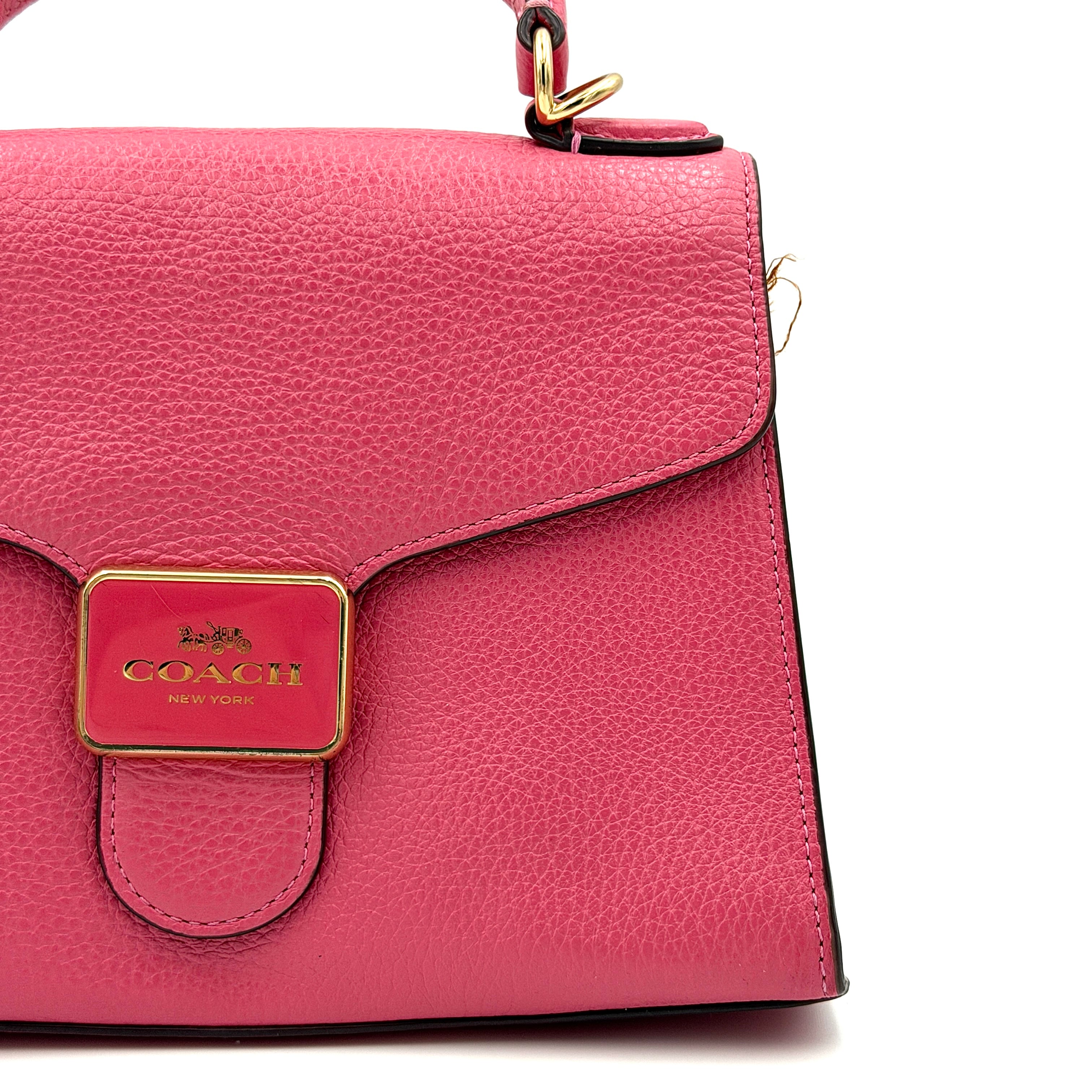Coach Pepper Satchel in bold pink pebbled leather, featuring a structured silhouette and gold logo push-lock hardware.