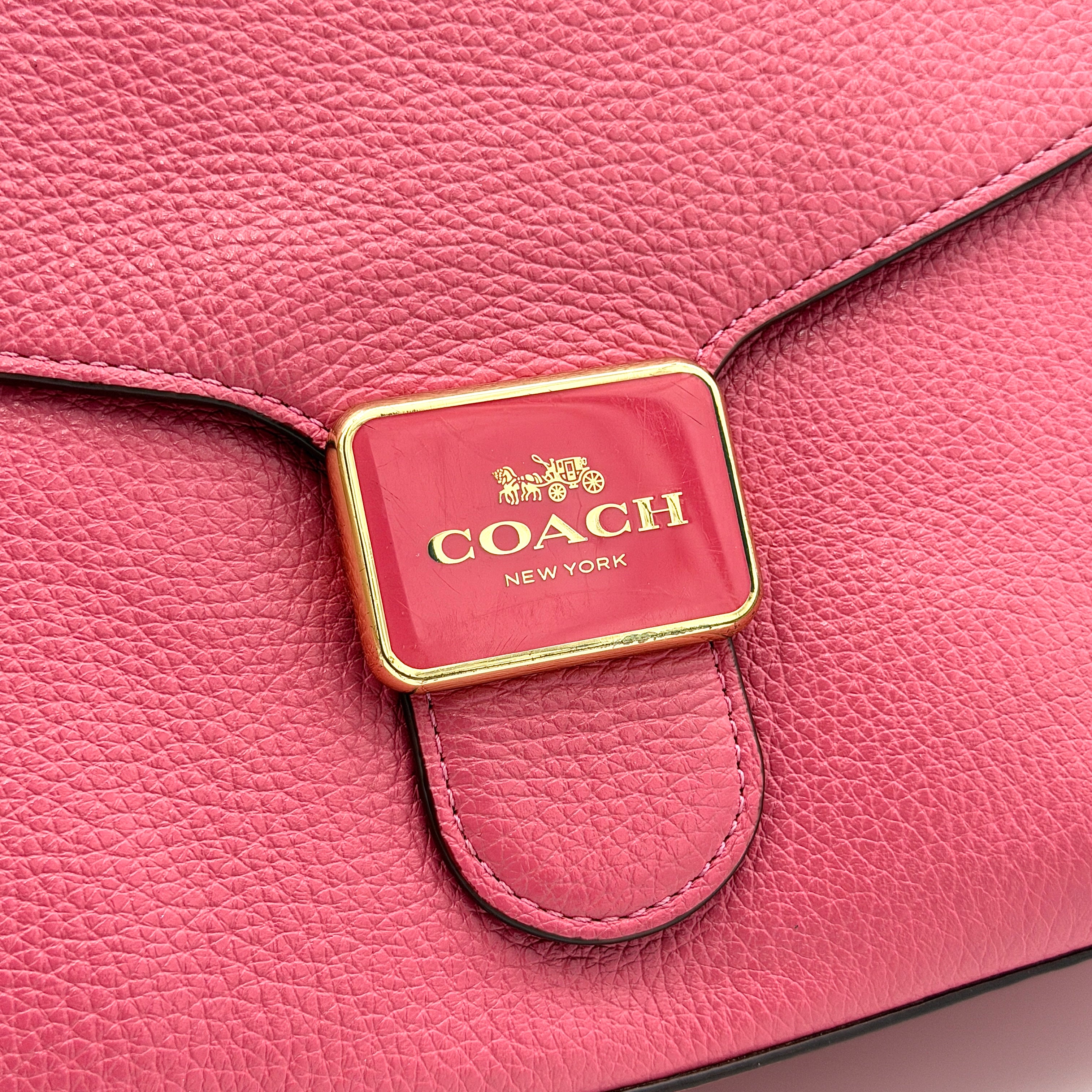 Coach Pepper Satchel in bold pink pebbled leather, featuring a structured silhouette and gold logo push-lock hardware.