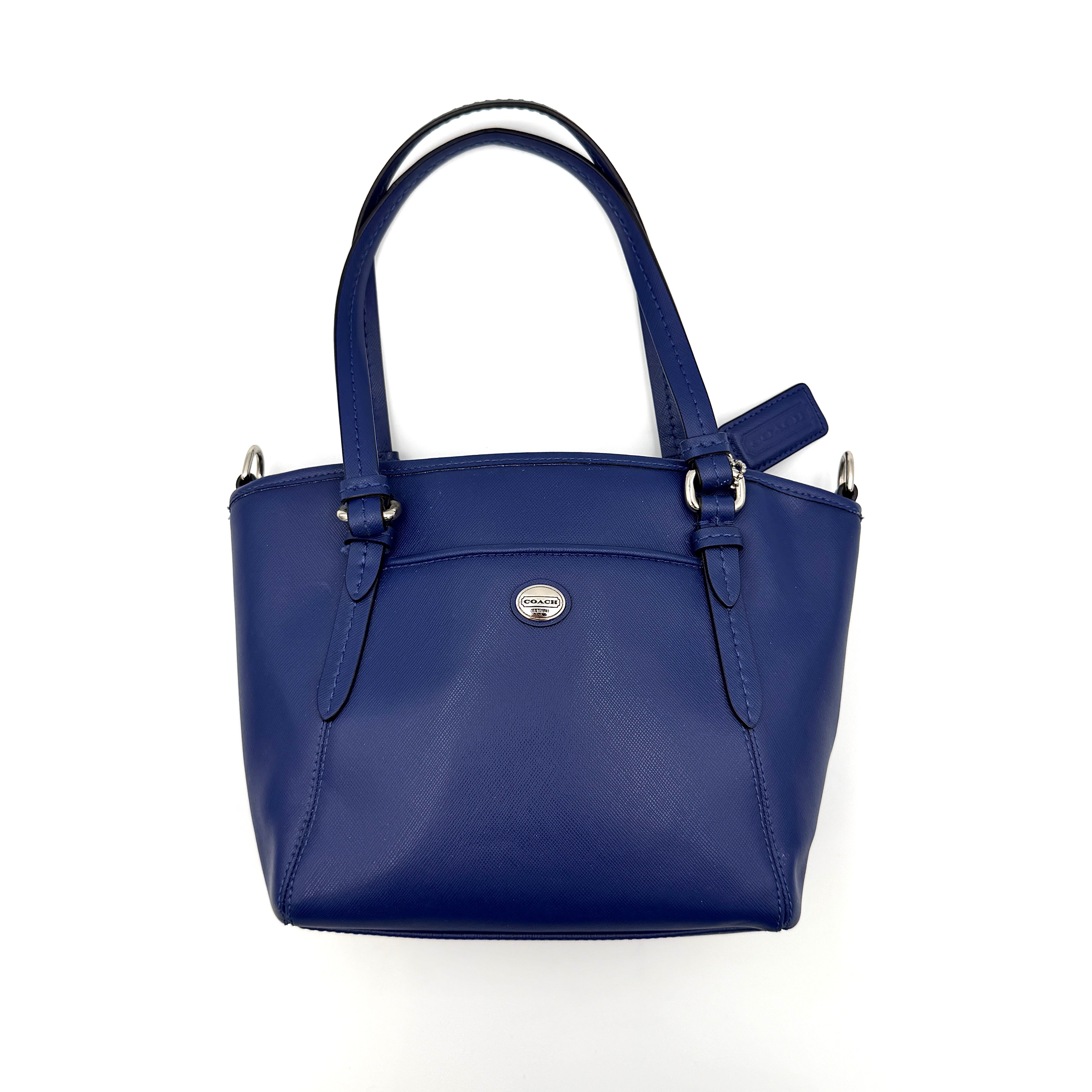 A structured cobalt blue Coach tote bag with silver hardware, dual handles, and an optional crossbody strap, displayed against a clean background.