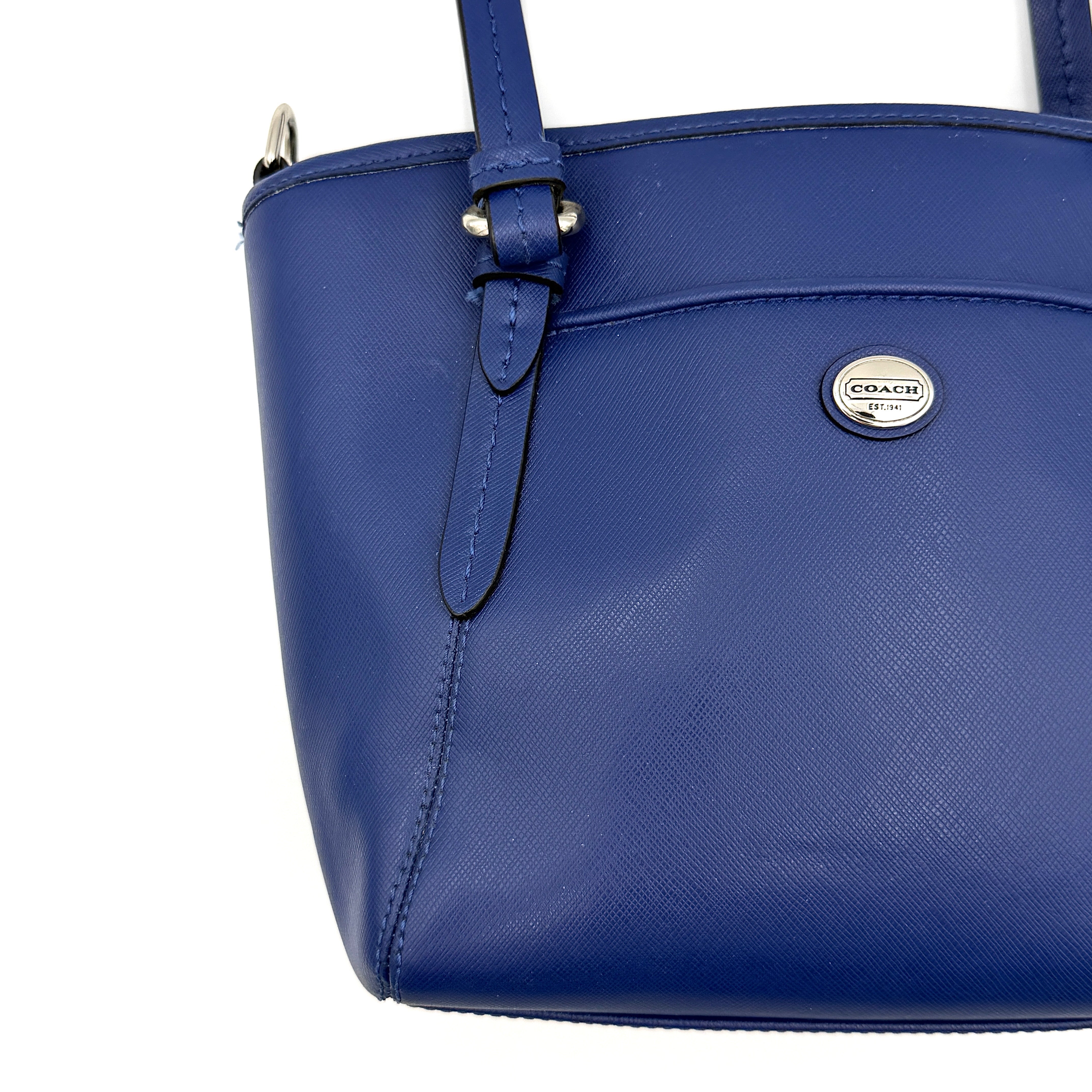 A structured cobalt blue Coach tote bag with silver hardware, dual handles, and an optional crossbody strap, displayed against a clean background.