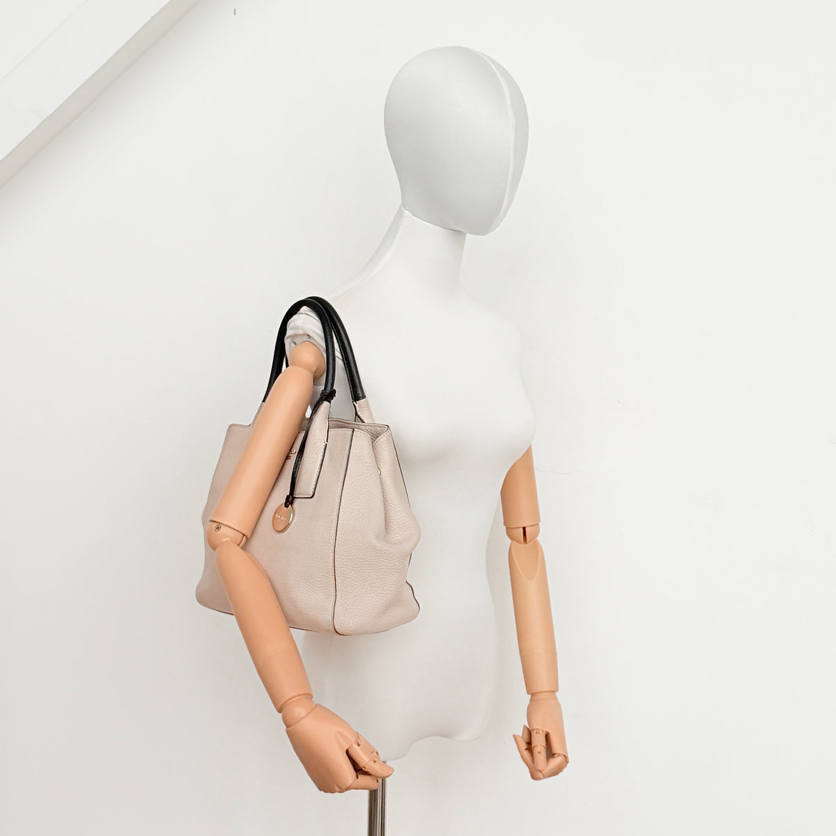 Kate Spade New York beige leather satchel with black handles, gold medallion, and grained texture against a white background.