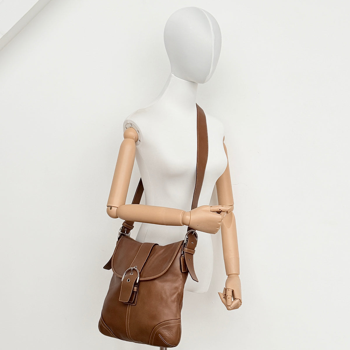 Coach Soho Buckle Flap Crossbody Bag in brown leather with buckle flap and adjustable strap, displayed on white background.