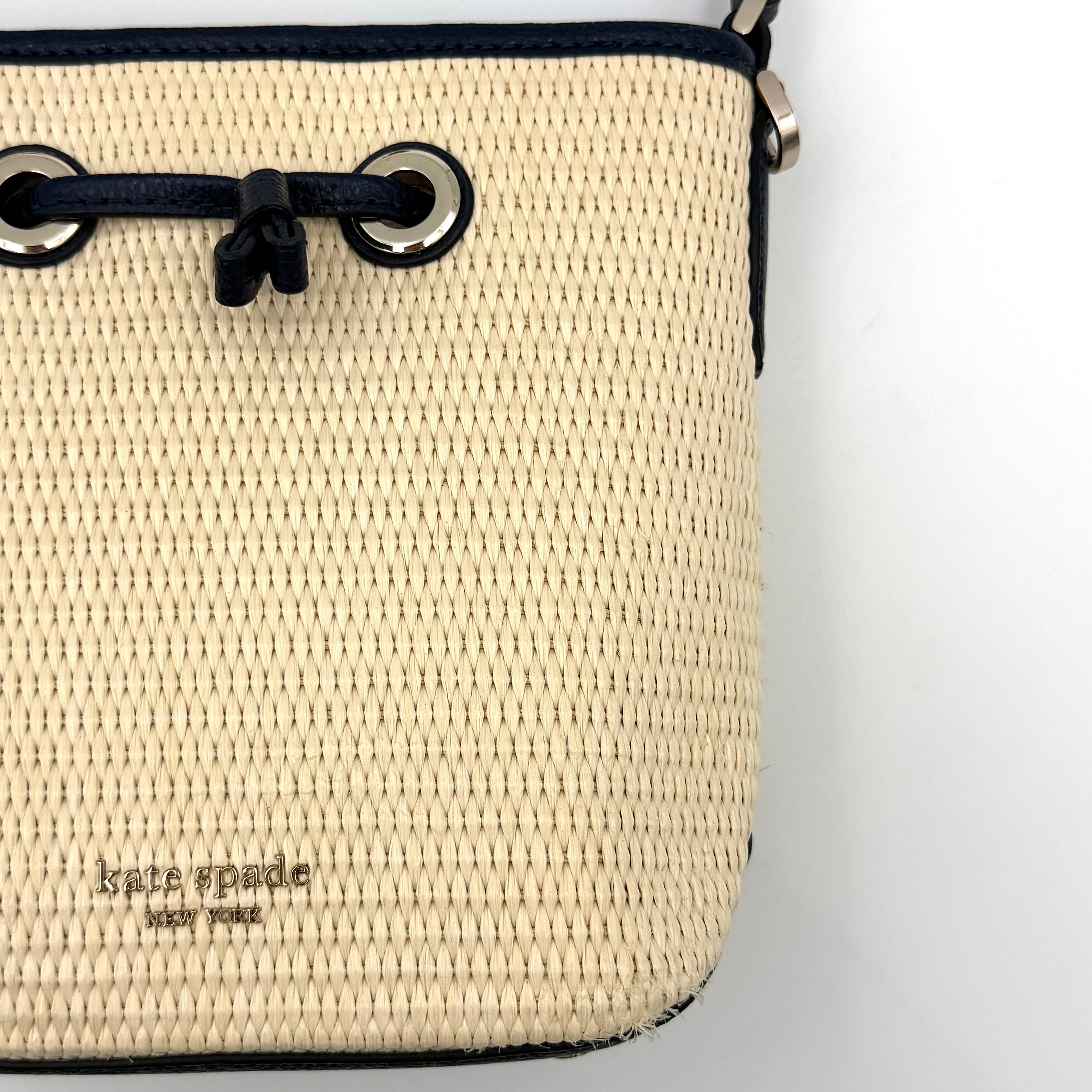 Front view of the Kate Spade Eva Straw Bucket Bag in cream, with navy leather trim and silver-tone hardware.