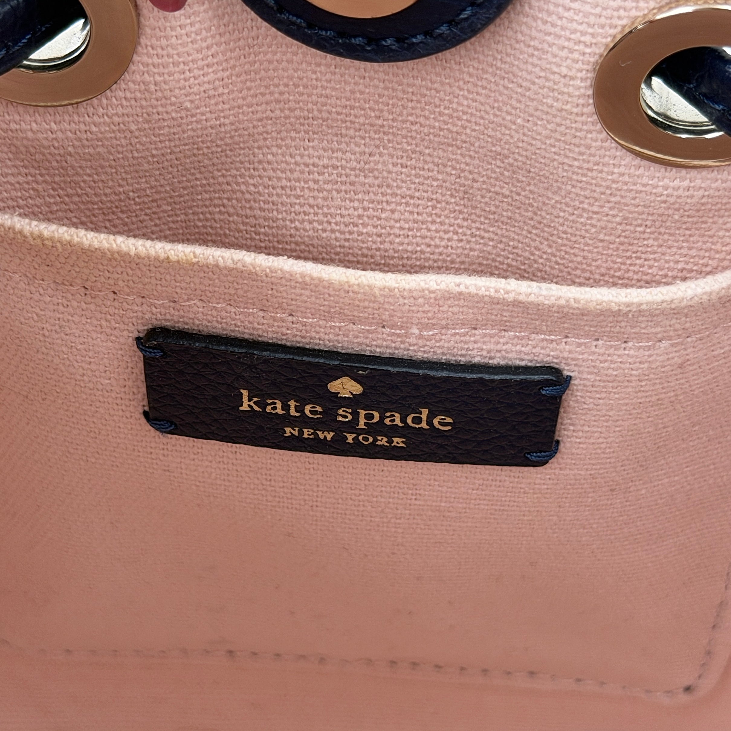 Front view of the Kate Spade Eva Straw Bucket Bag in cream, with navy leather trim and silver-tone hardware.