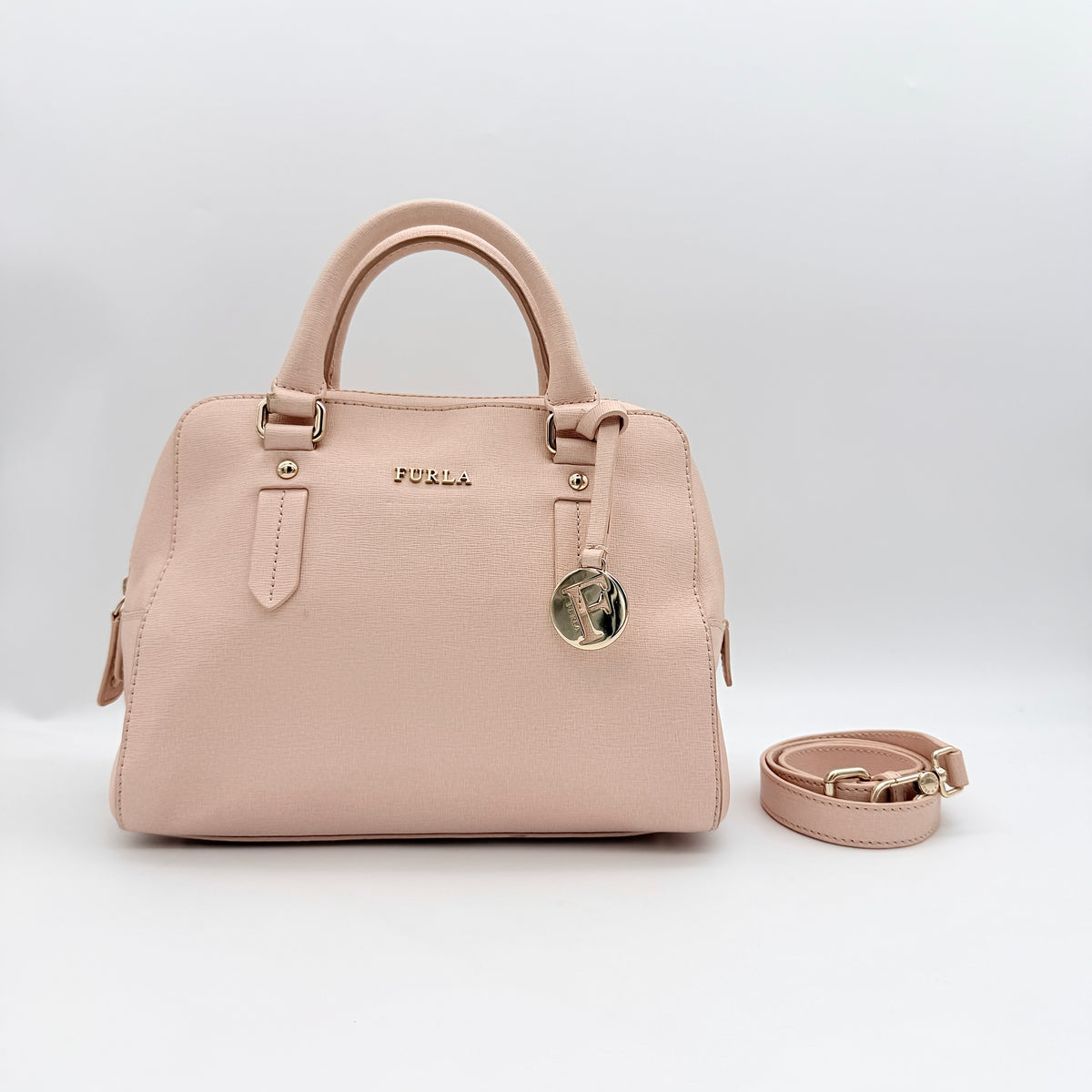 Furla Elena 2Way Saffiano leather satchel in beige with gold-tone hardware and removable strap, displayed on Furla-branded dust bag.