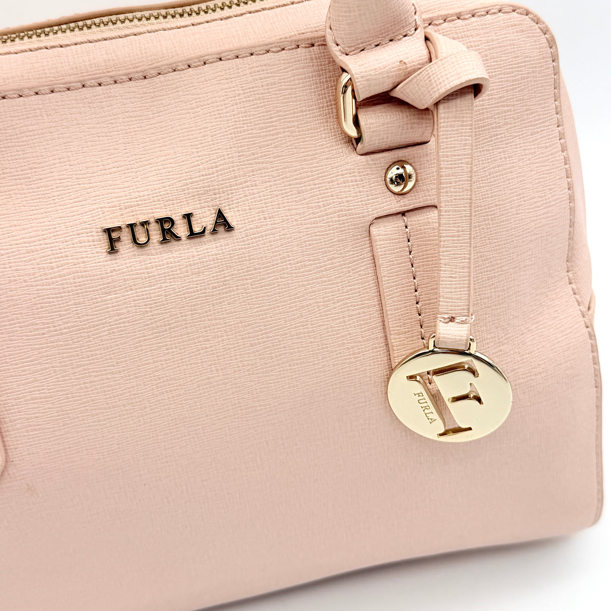 Furla Elena 2Way Saffiano leather satchel in beige with gold-tone hardware and removable strap, displayed on Furla-branded dust bag.