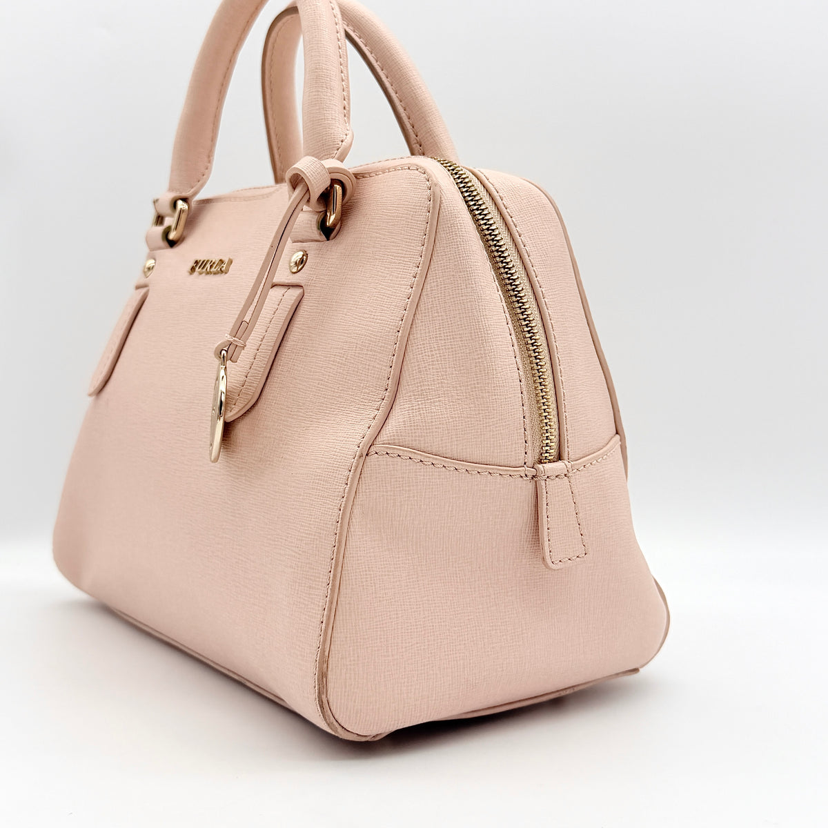 Furla Elena 2Way Saffiano leather satchel in beige with gold-tone hardware and removable strap, displayed on Furla-branded dust bag.
